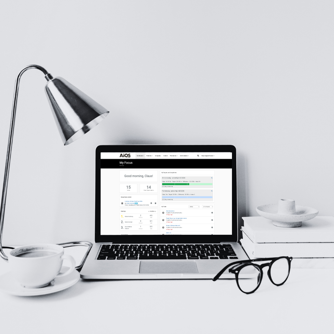 A minimalist workspace featuring a laptop displaying a dashboard, a white ceramic cup with saucer, a pair of black glasses, a stack of books with a ceramic dish on top, a modern desk lamp, and a white background.