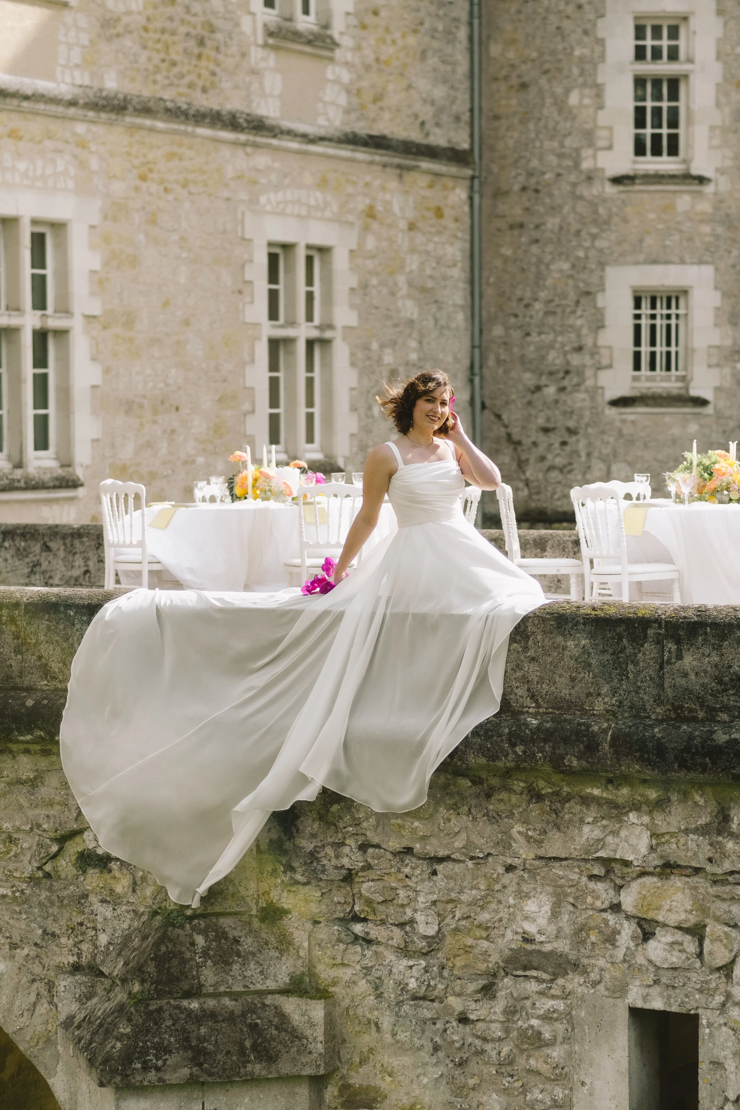 Une marriée assise sur un pont qui laisse pendre sa robe dans le vide