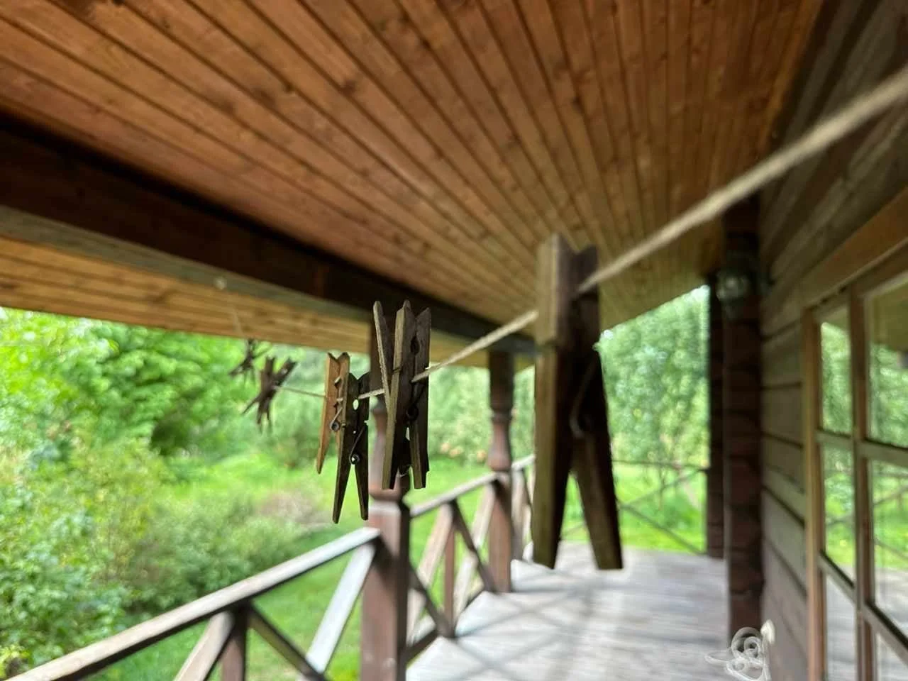 Clothespins hanging on a clothesline on a wooden porch with greenery in the background.