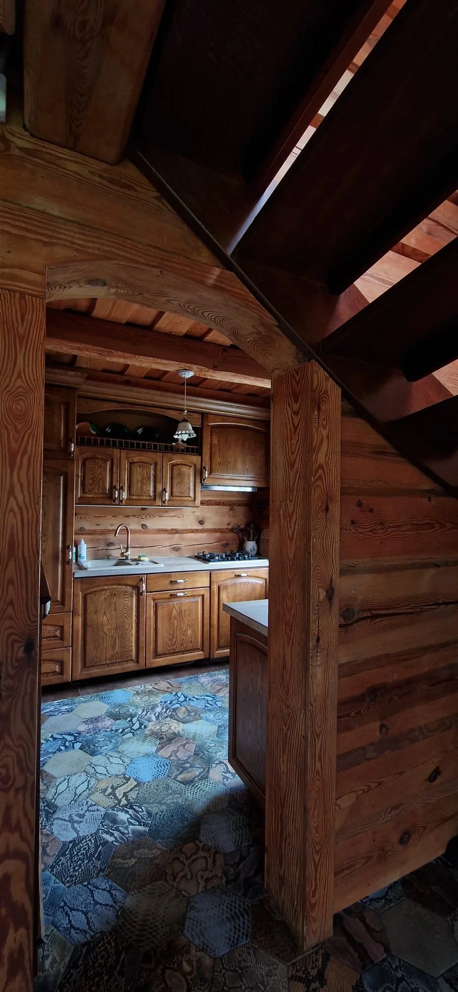 Wood-paneled rustic kitchen with wooden cabinets, a gas stove, a white countertop, and a patterned tile floor.