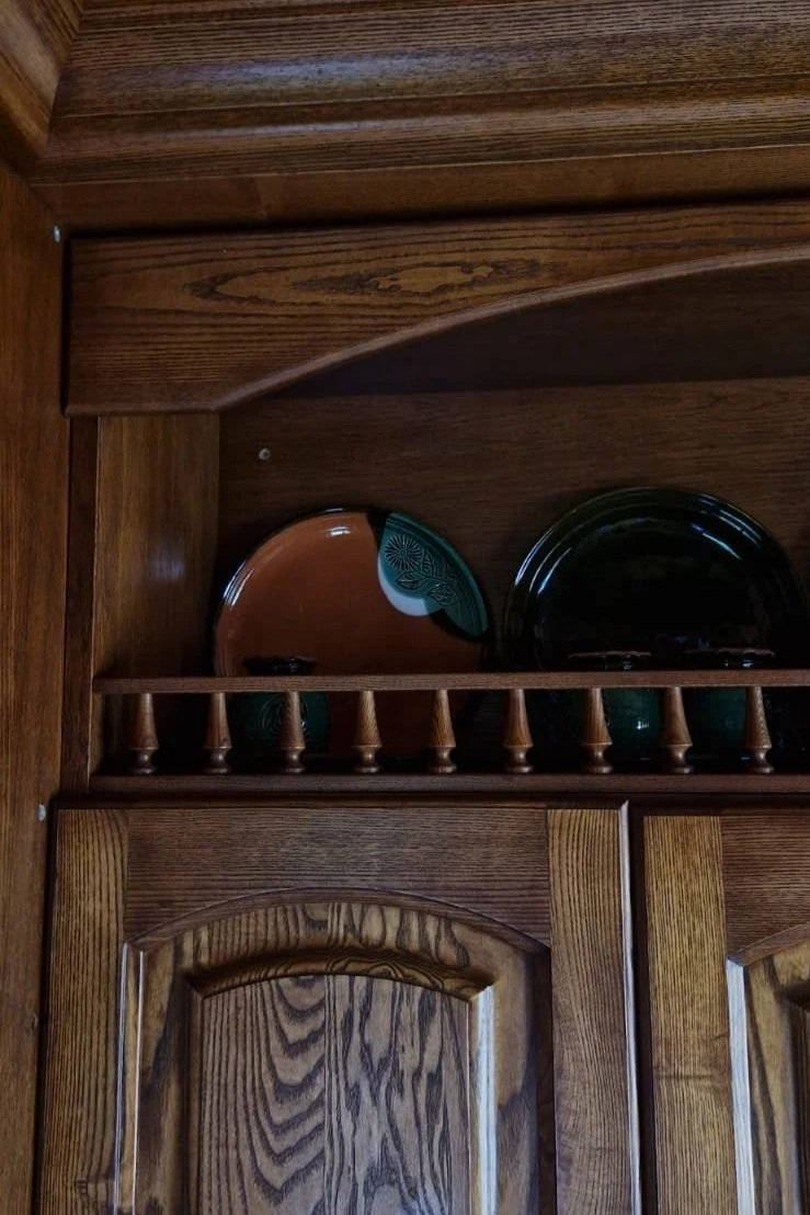 Wooden kitchen cabinet with decorative plate and dark plate inside an upper shelf.