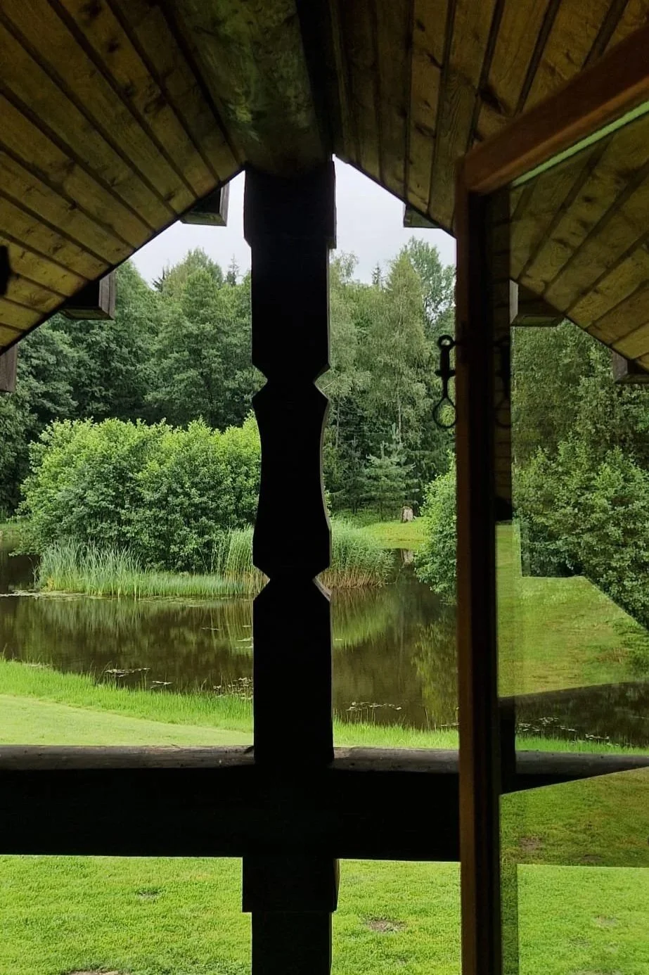 View from a porch or window looking out over a pond surrounded by lush green trees and grass.