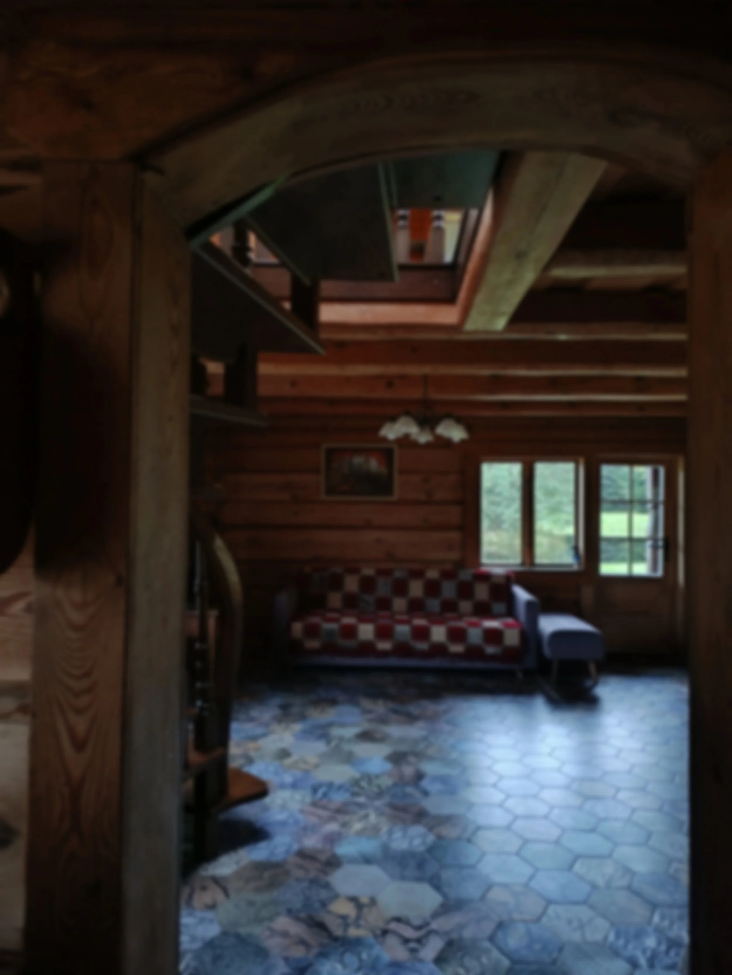 Interior of a rustic wooden cabin living room with windows, a patterned couch, and a tiled floor.
