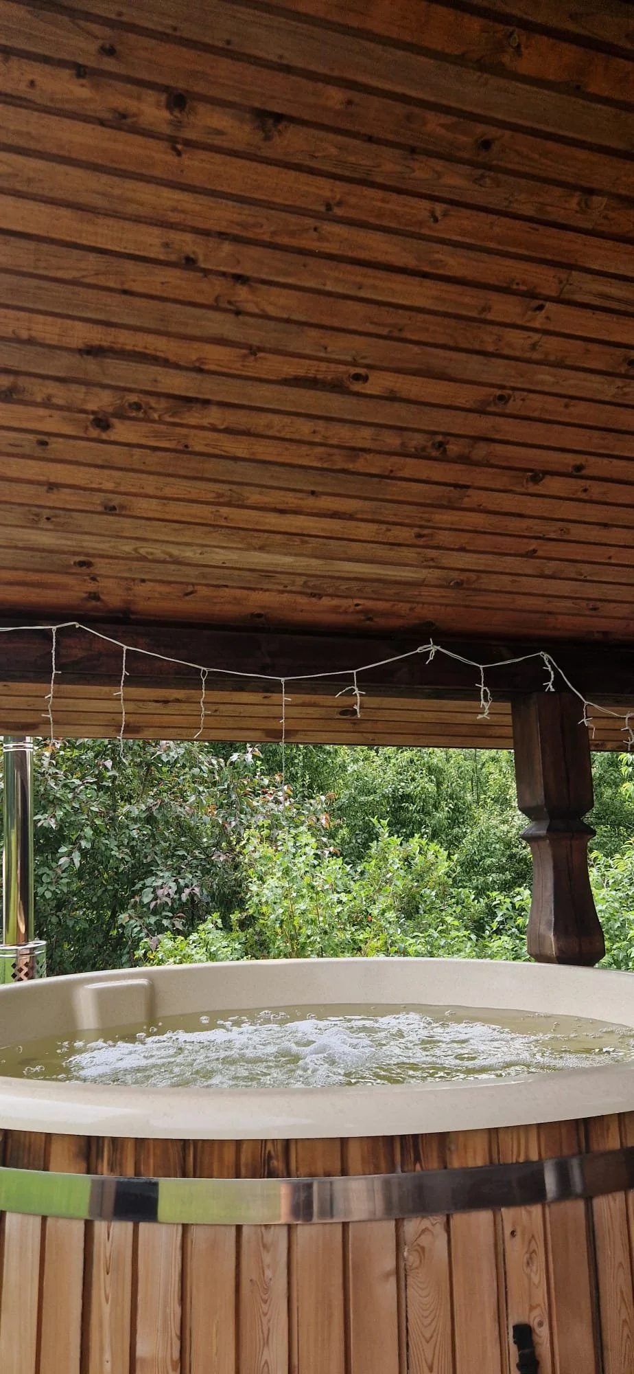 A hot tub with bubbling water on a porch with a wooden ceiling and lush green trees in the background.