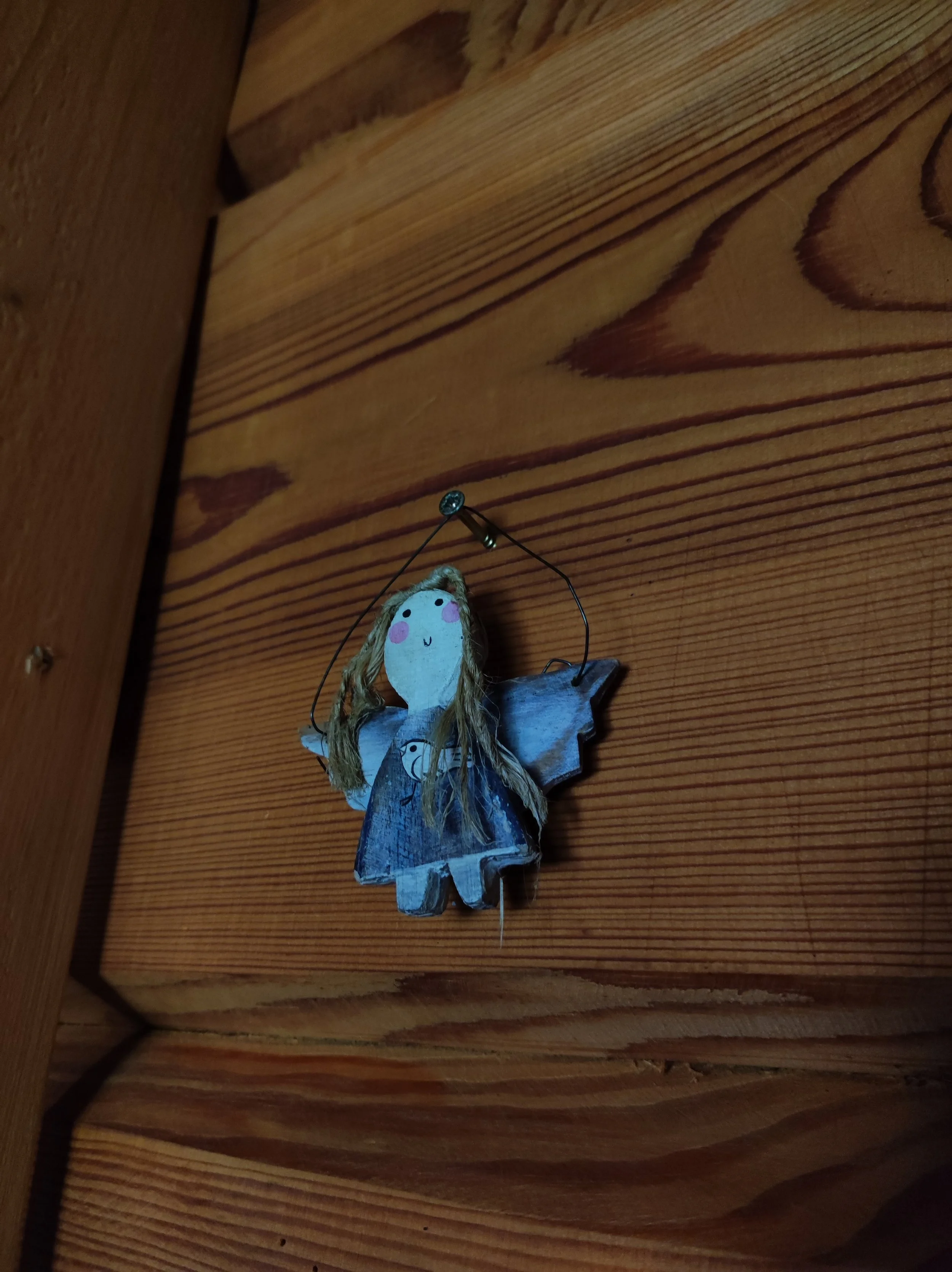Wooden wall with a small decorative angel ornament hanging from a nail.