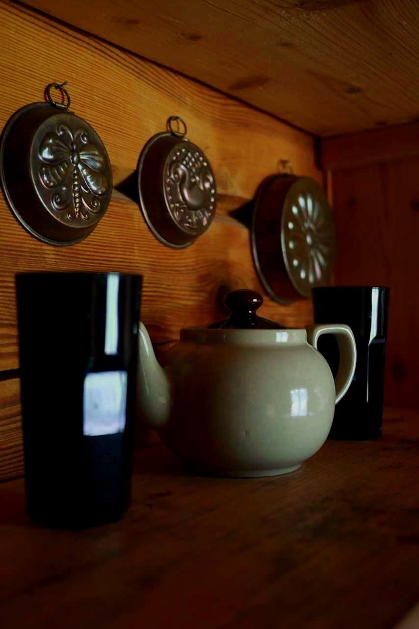 Decorative metal molds hung on a wooden wall, with a ceramic teapot and two black drinking glasses on a wooden surface.