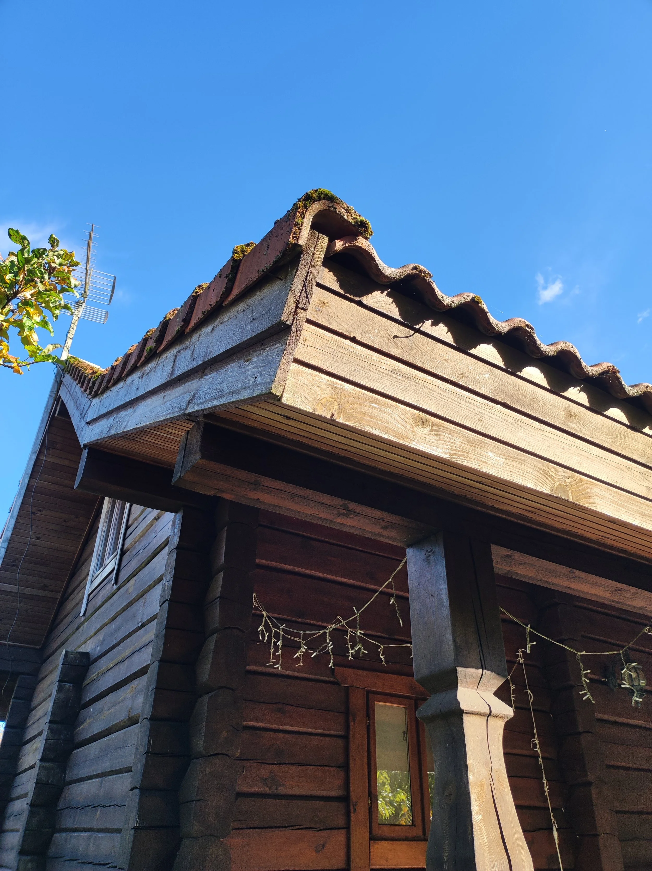 Close-up of a wooden house with a sloped tiled roof and decorative wooden beams, under a clear blue sky.