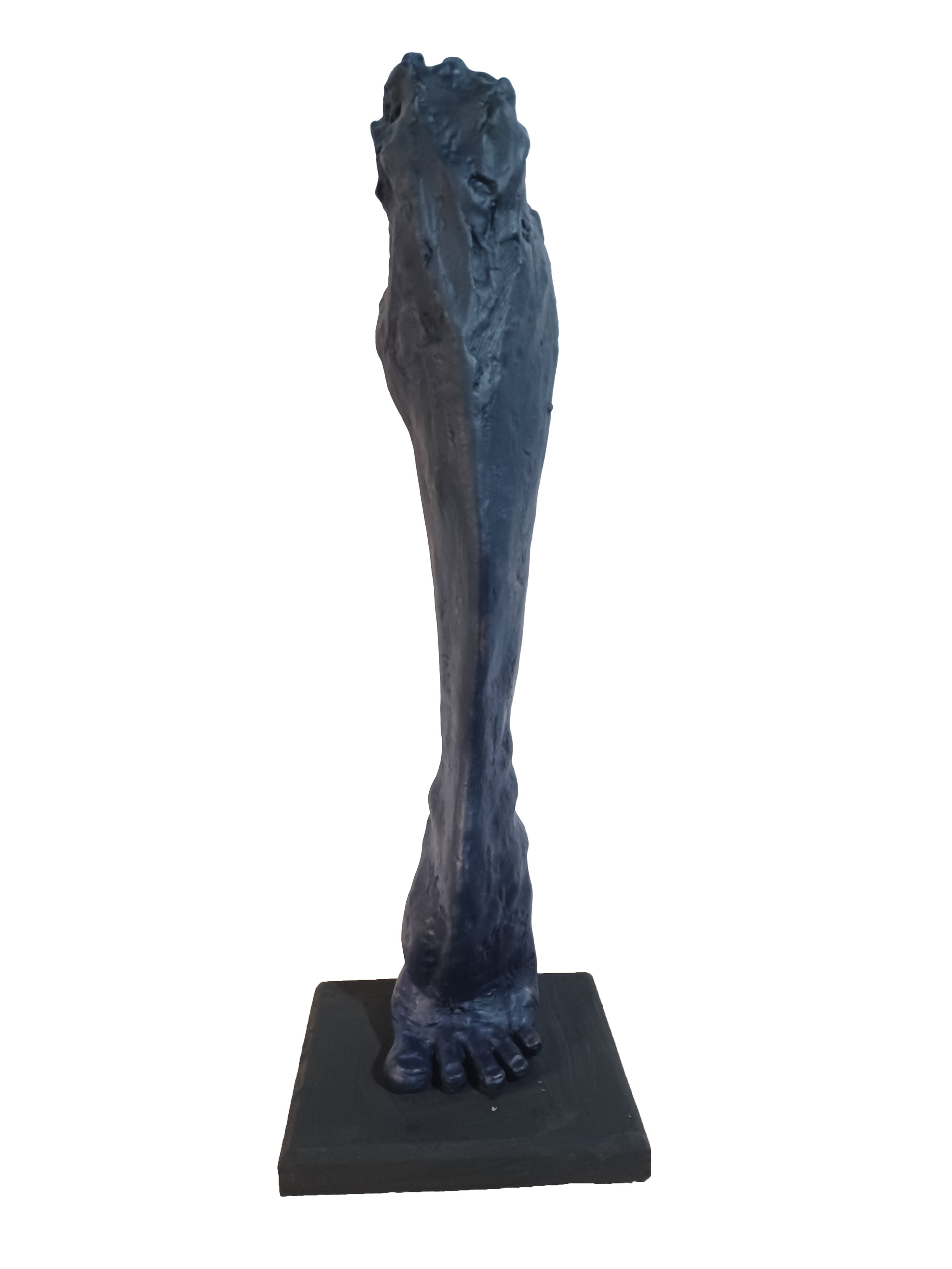 Sculpture of a human leg and foot in dark material on a square base.