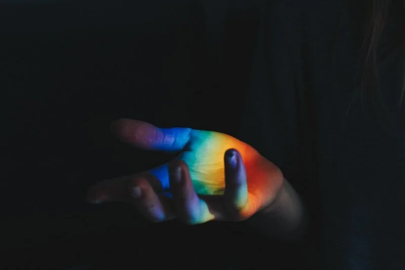 Rainbow light shines across open hand flowing Reiki