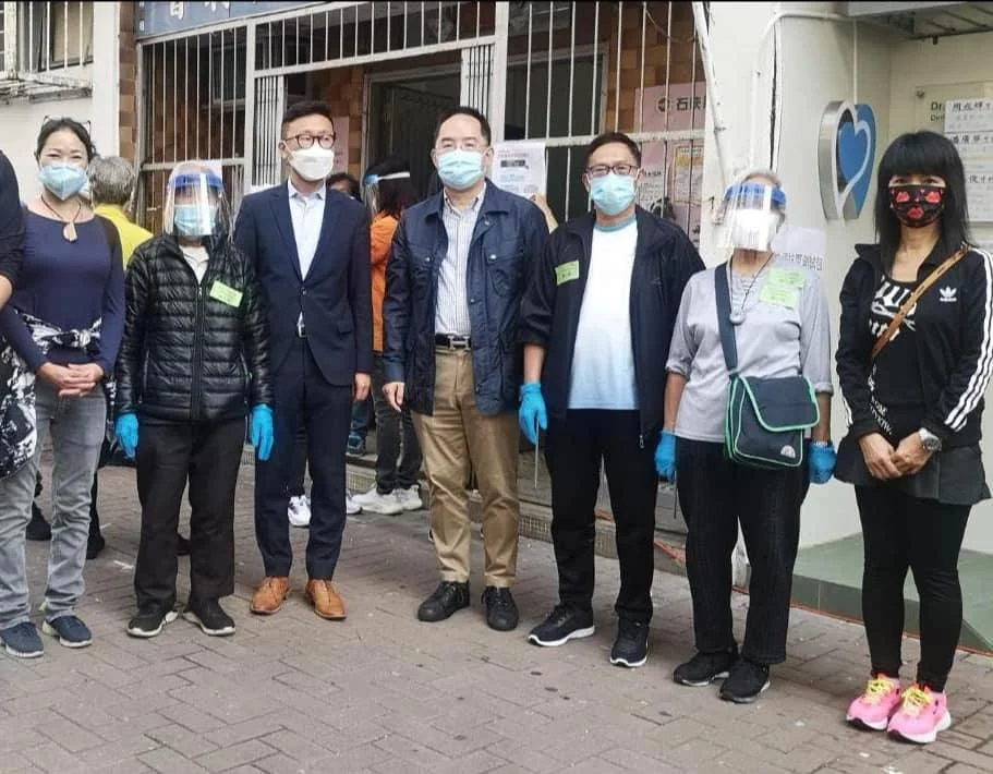 八人組戴著口罩與手套，站在建築物外的人行道上。