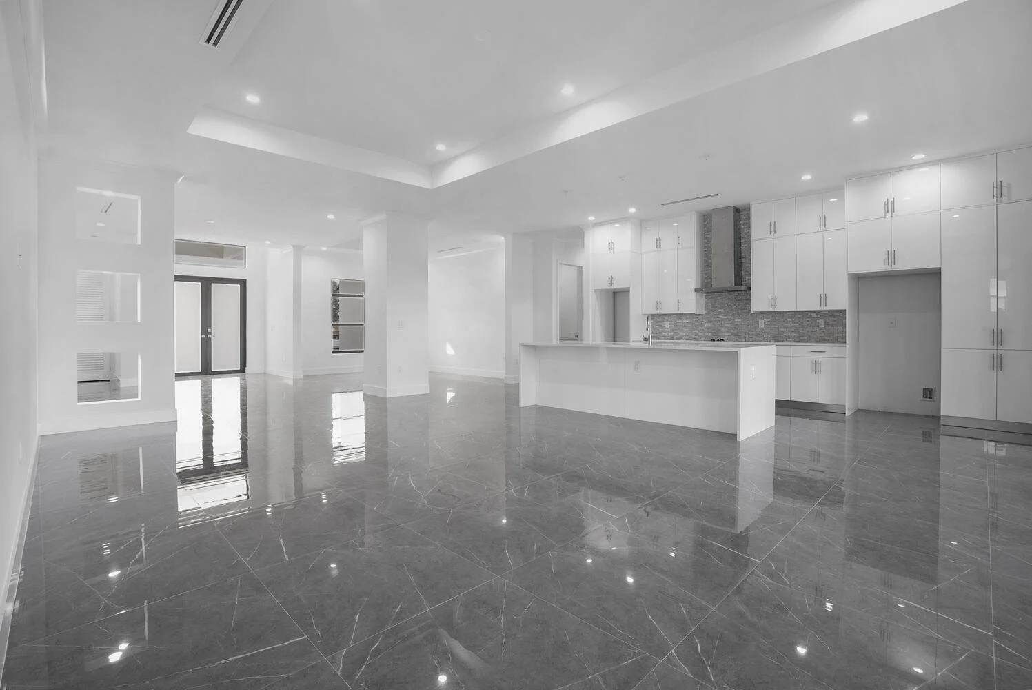 Empty modern kitchen and living space with glossy gray marble floors, white walls, cabinetry, and recessed ceiling lights.