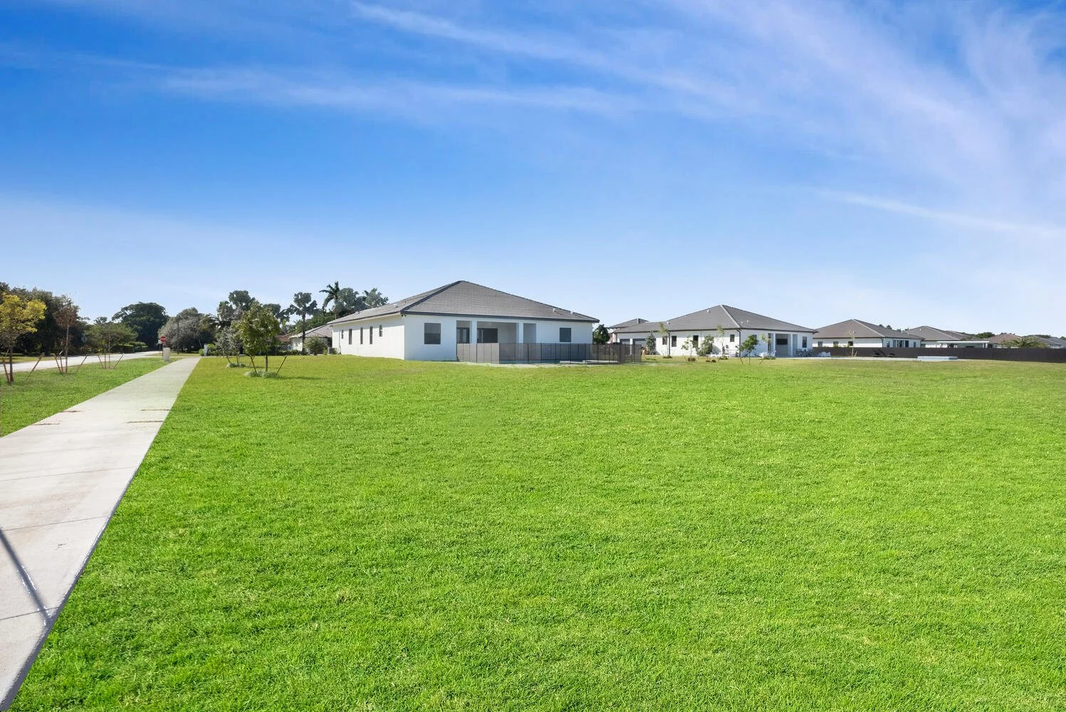 A suburban neighborhood with multiple white houses, green lawns, a sidewalk, and a blue sky.