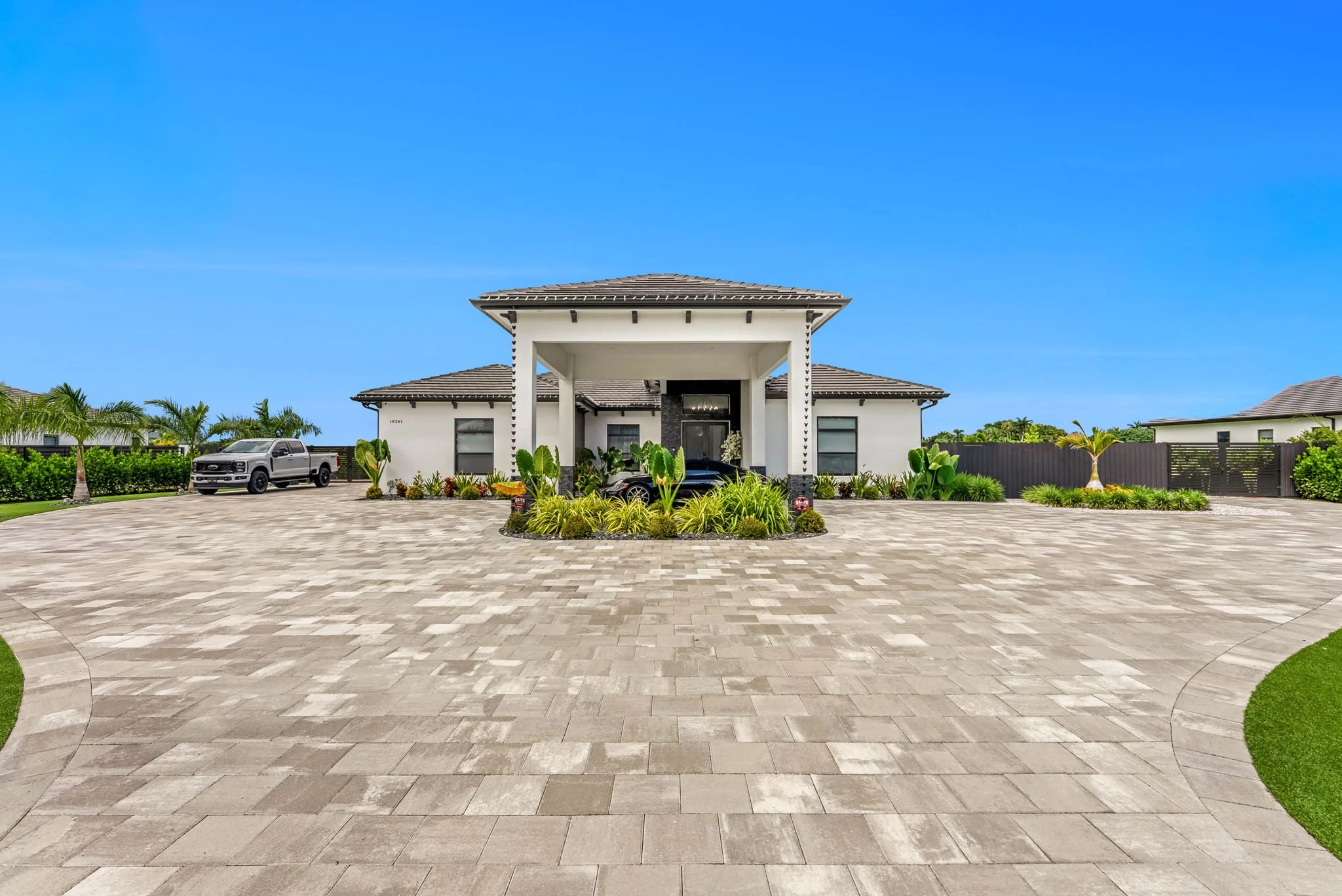 Front view of a modern house with a driveway, landscaping, and a pickup truck parked outside, under a clear blue sky.
