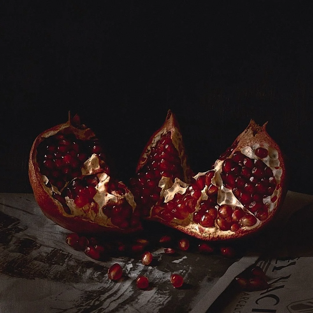 A pomegranate fruit split open, exposing red seeds inside, placed on a dark surface with some seeds scattered around.