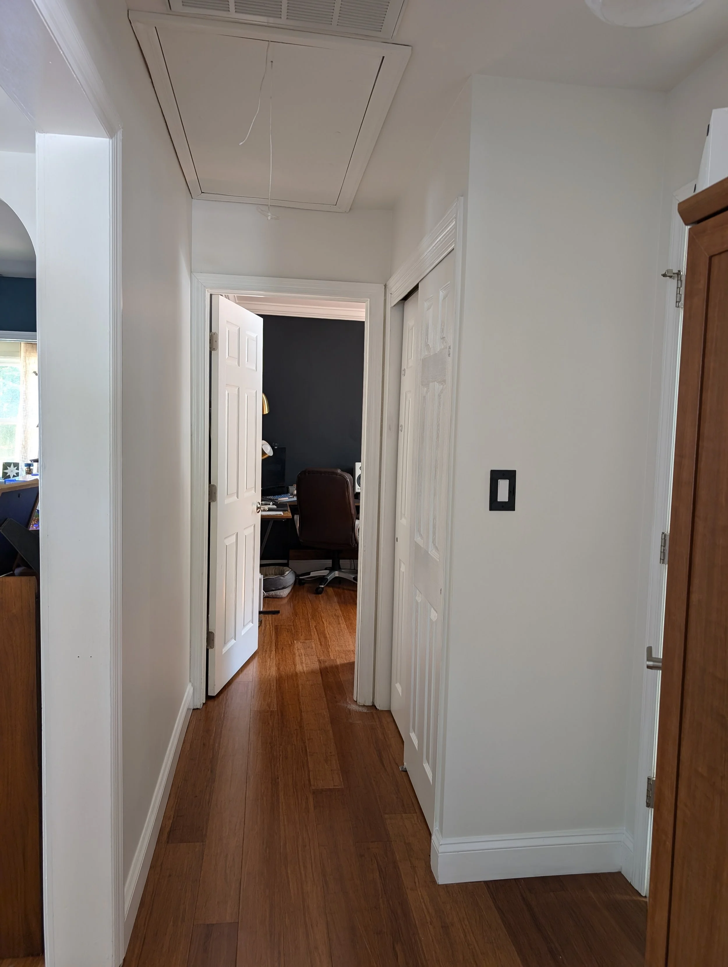 after photo of small hallway. all walls refreshed with a neutral white color on walls and ceiling. More light pours into area now. Door at end of hallway is open.
