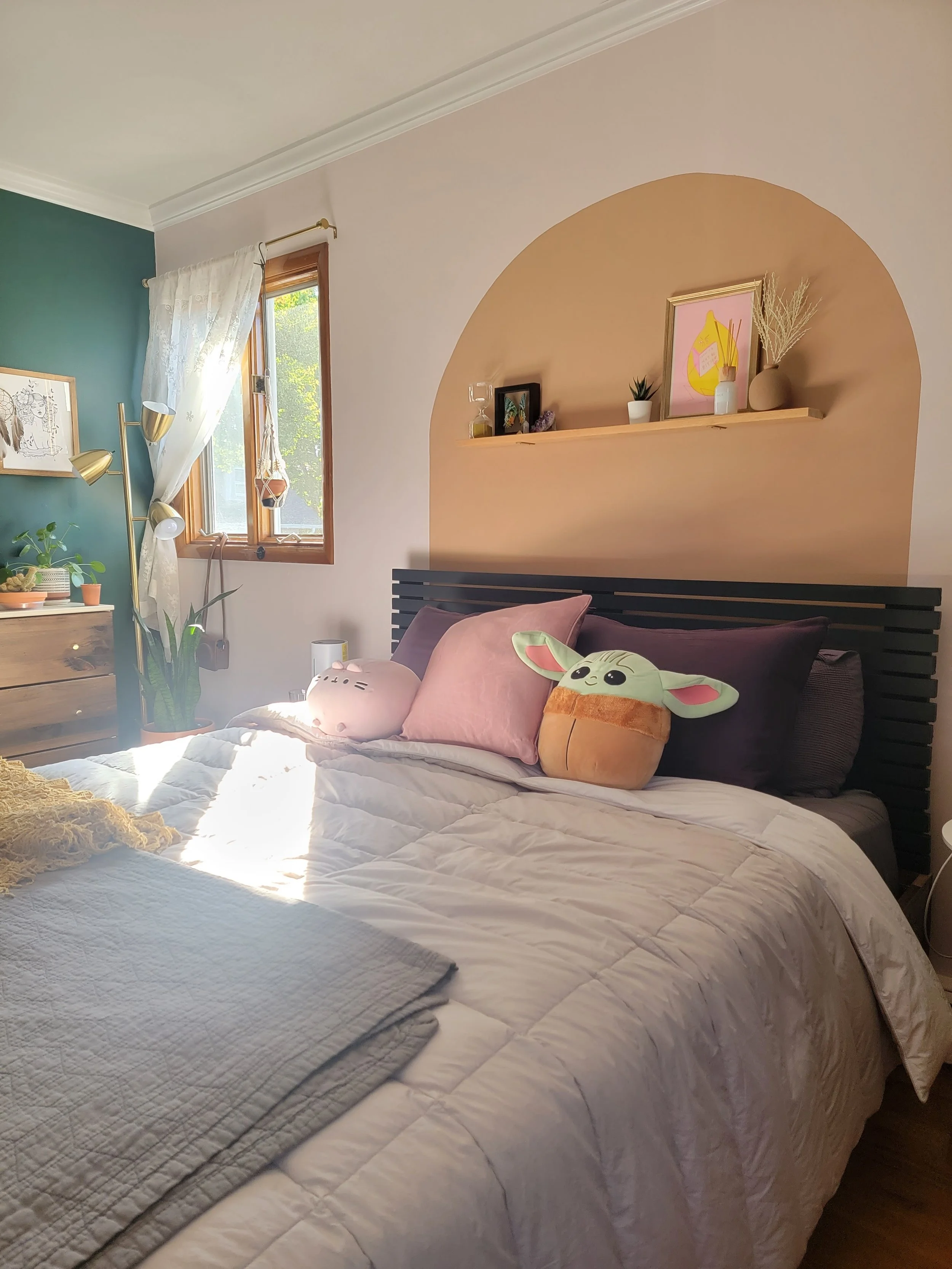 a cozy bedroom with a light pink accent wall and gold painted arch above the bedframe