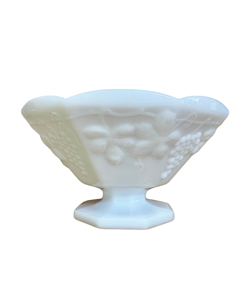 Front view of a vintage Anchor Hocking white milk glass pedestal bowl with raised grapes and a scalloped rim