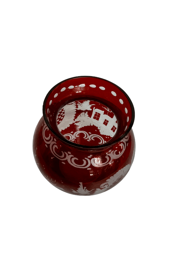 High-angle view of a vintage ruby-flashed glass vase showing its cut-to-clear cottage scene and decorative rim dots