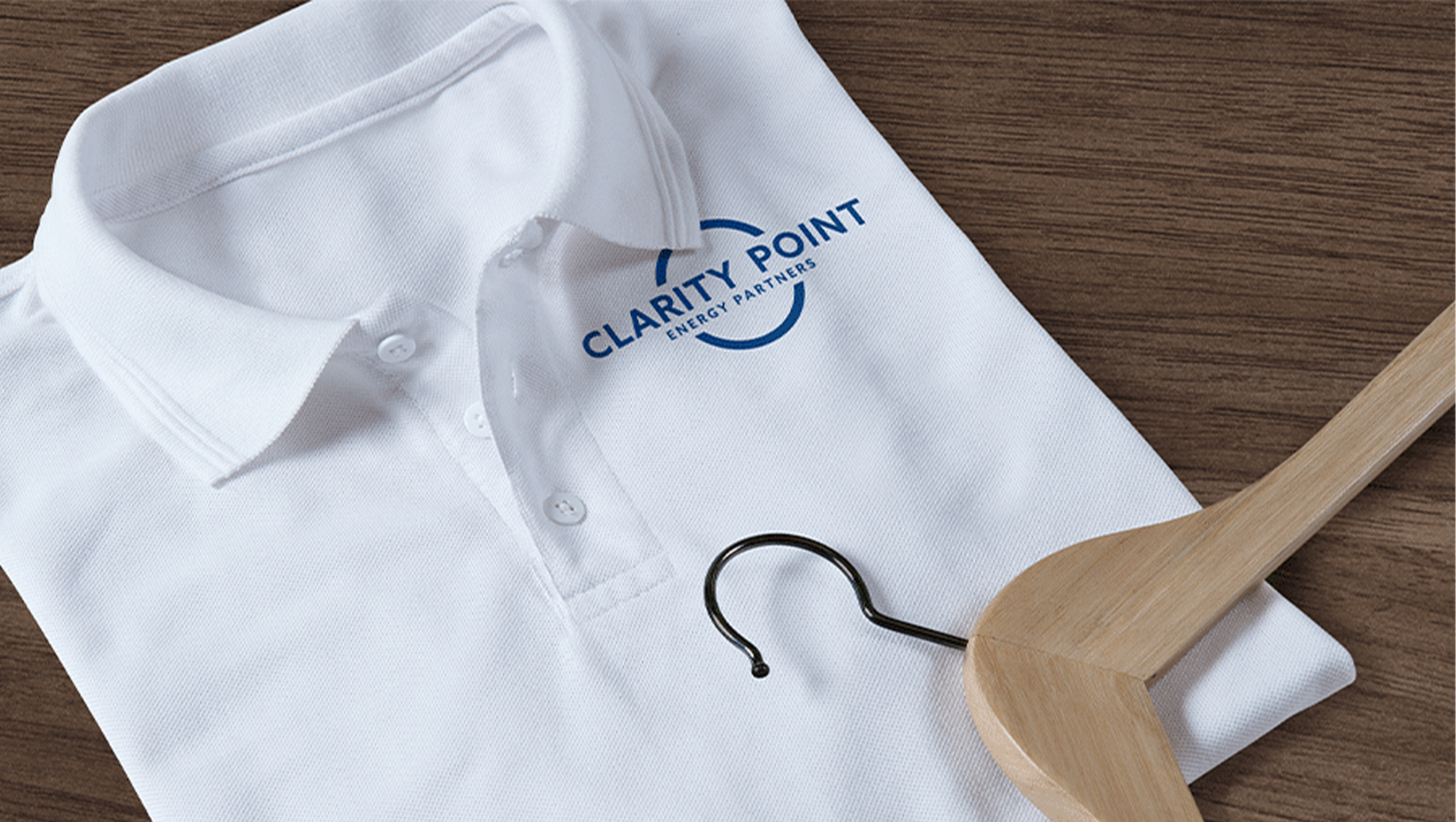 Folded white polo shirt with Clarity Point logo and a wooden hanger