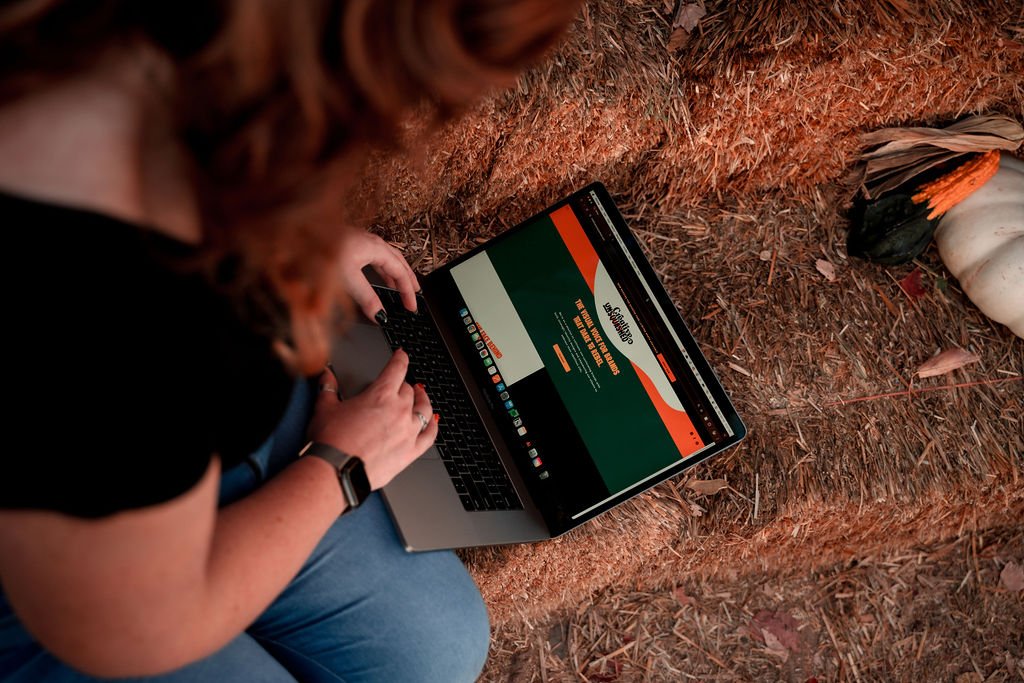 Felicia sitting on hay with laptop showing old Creative Unsquashed website