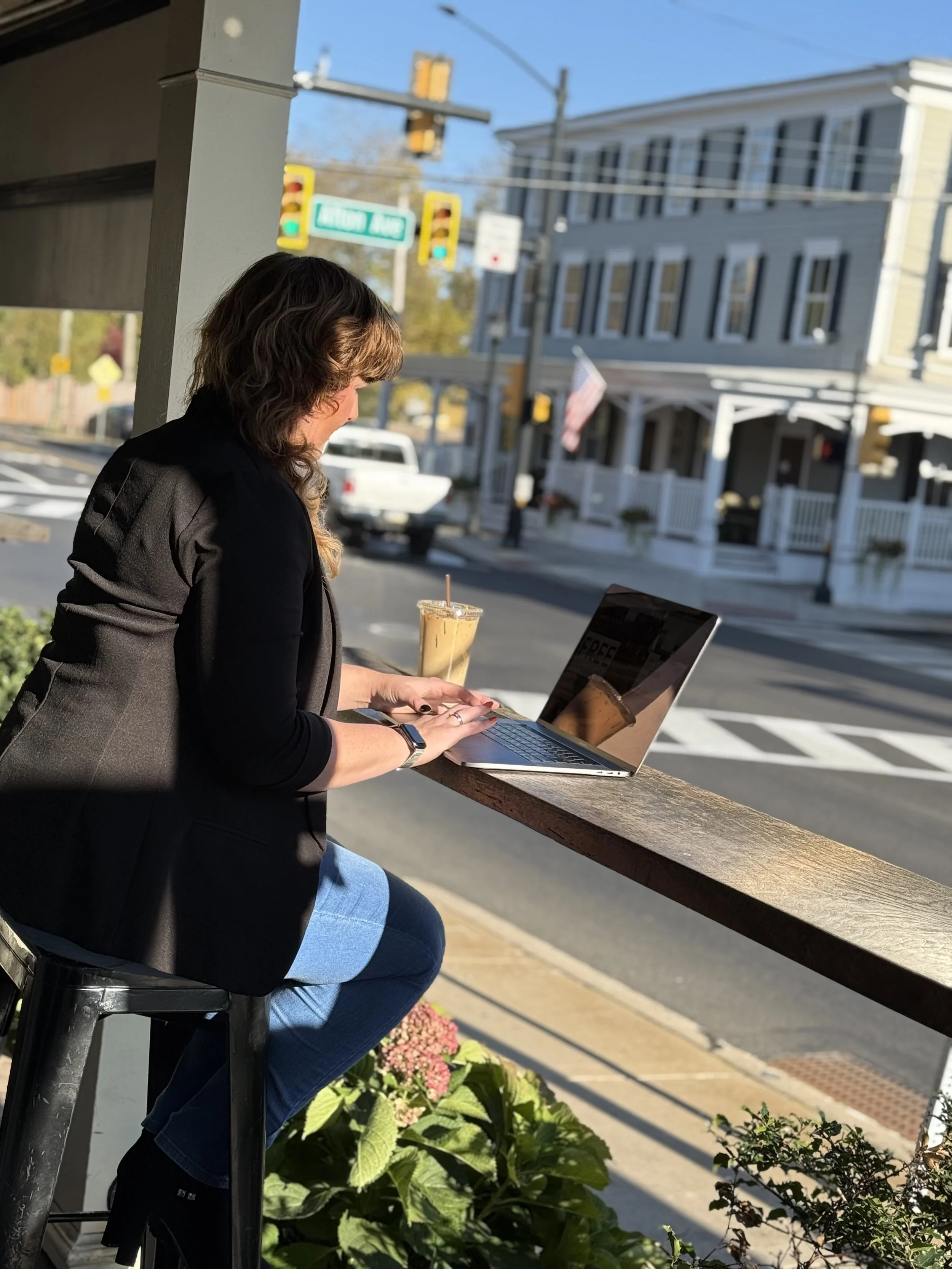 Photo of Felicia sitting outside of coffee shop with laptop, blurred street view background