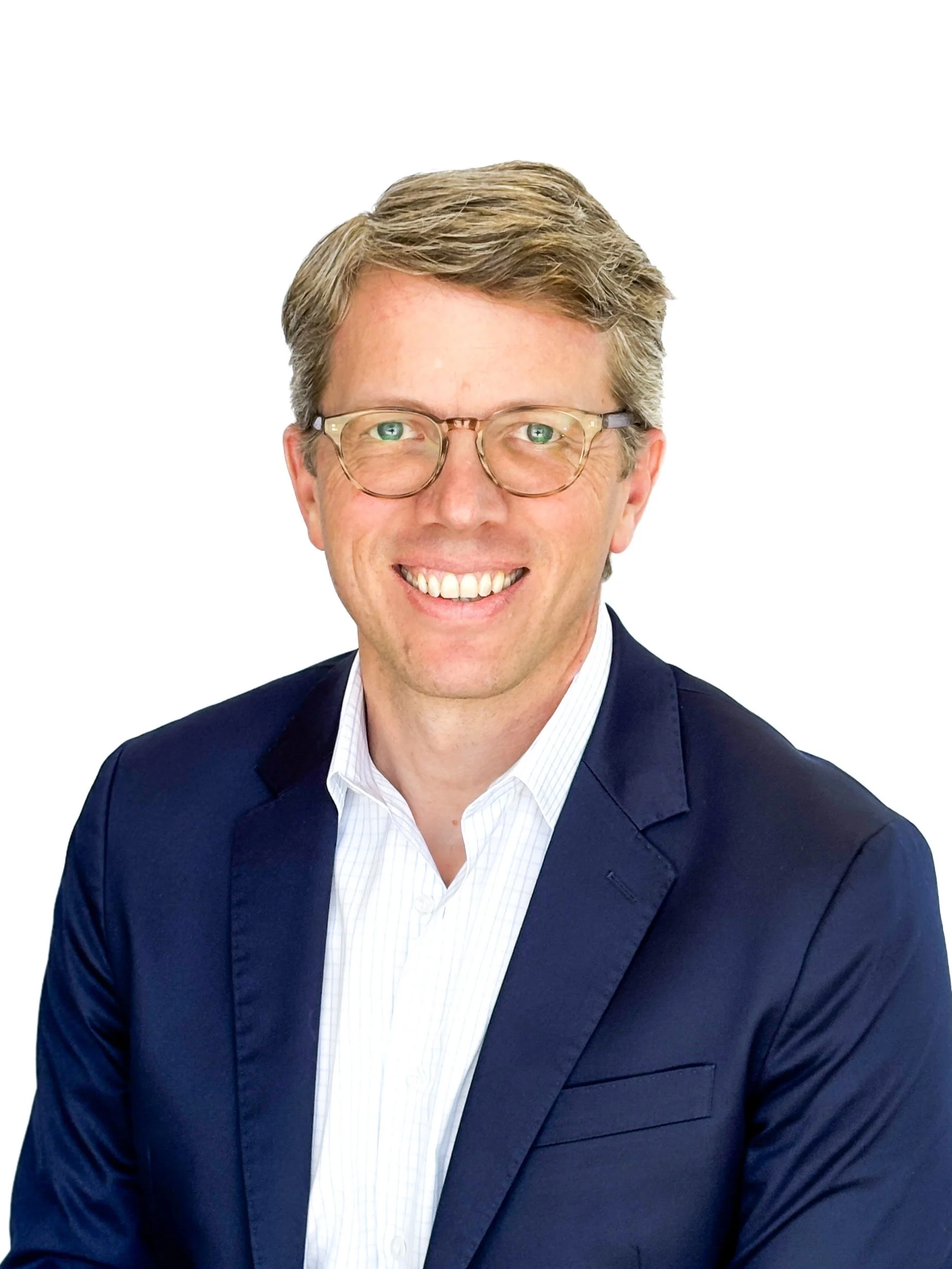 A professional man with light brown hair, glasses, a white shirt, and a navy blazer, smiling at the camera against a plain white background.
