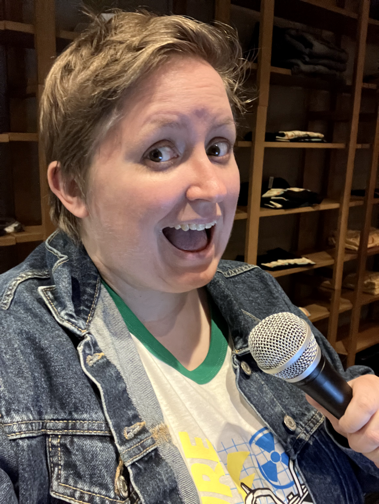 Ashley, wearing a t-shirt and jean jacket, working the mic at a recent event.