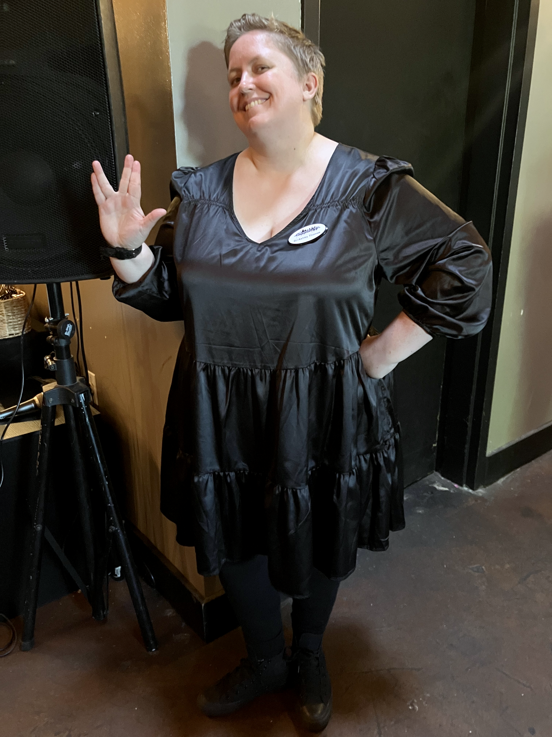 Ashley dressed in black giving the "Live Long and Prosper" hand gesture at an event. She is wearing a name tag that says "DJ Ashley Thomas."