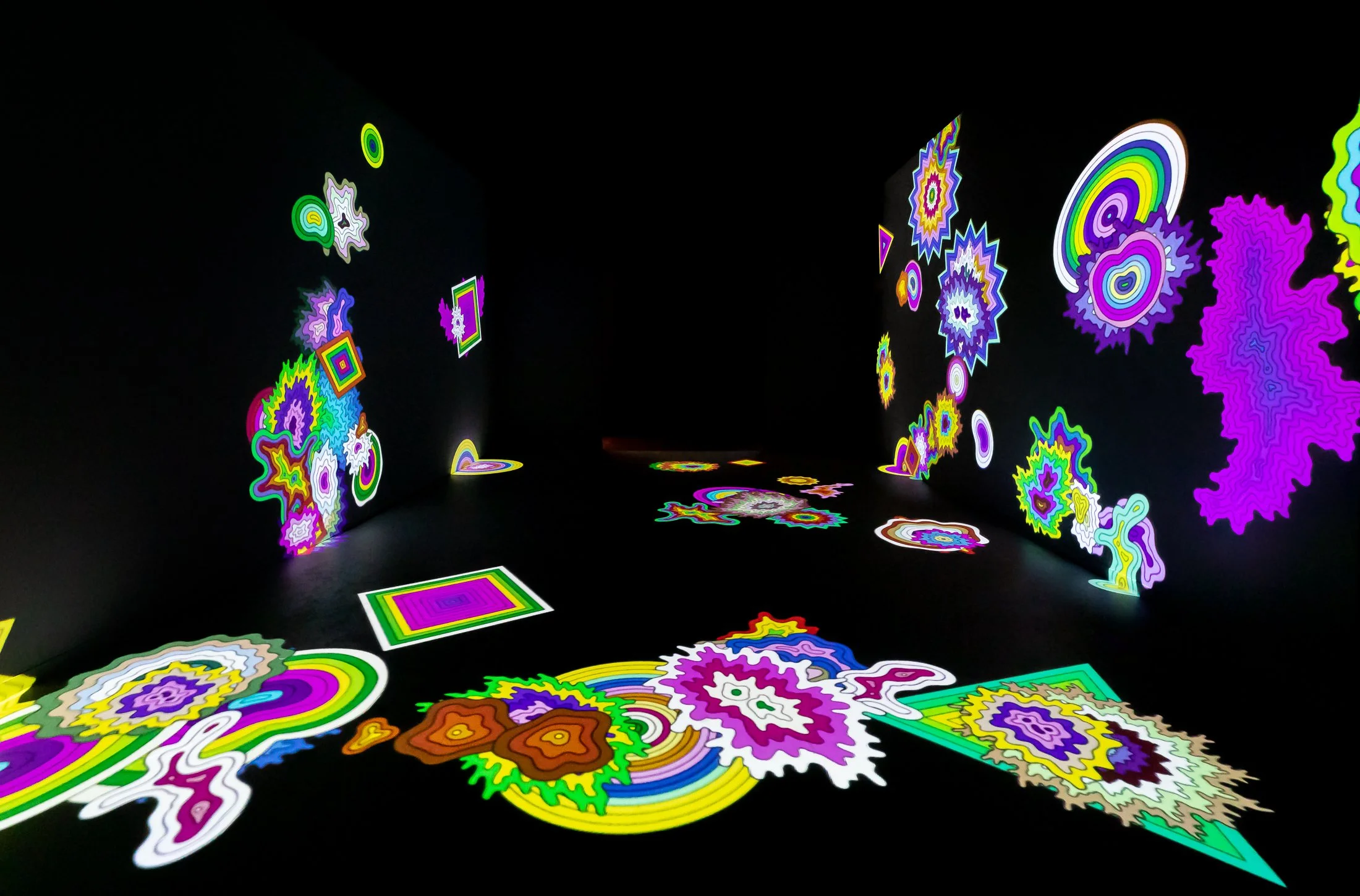 Colorful glowing abstract shapes projected on black walls and floor