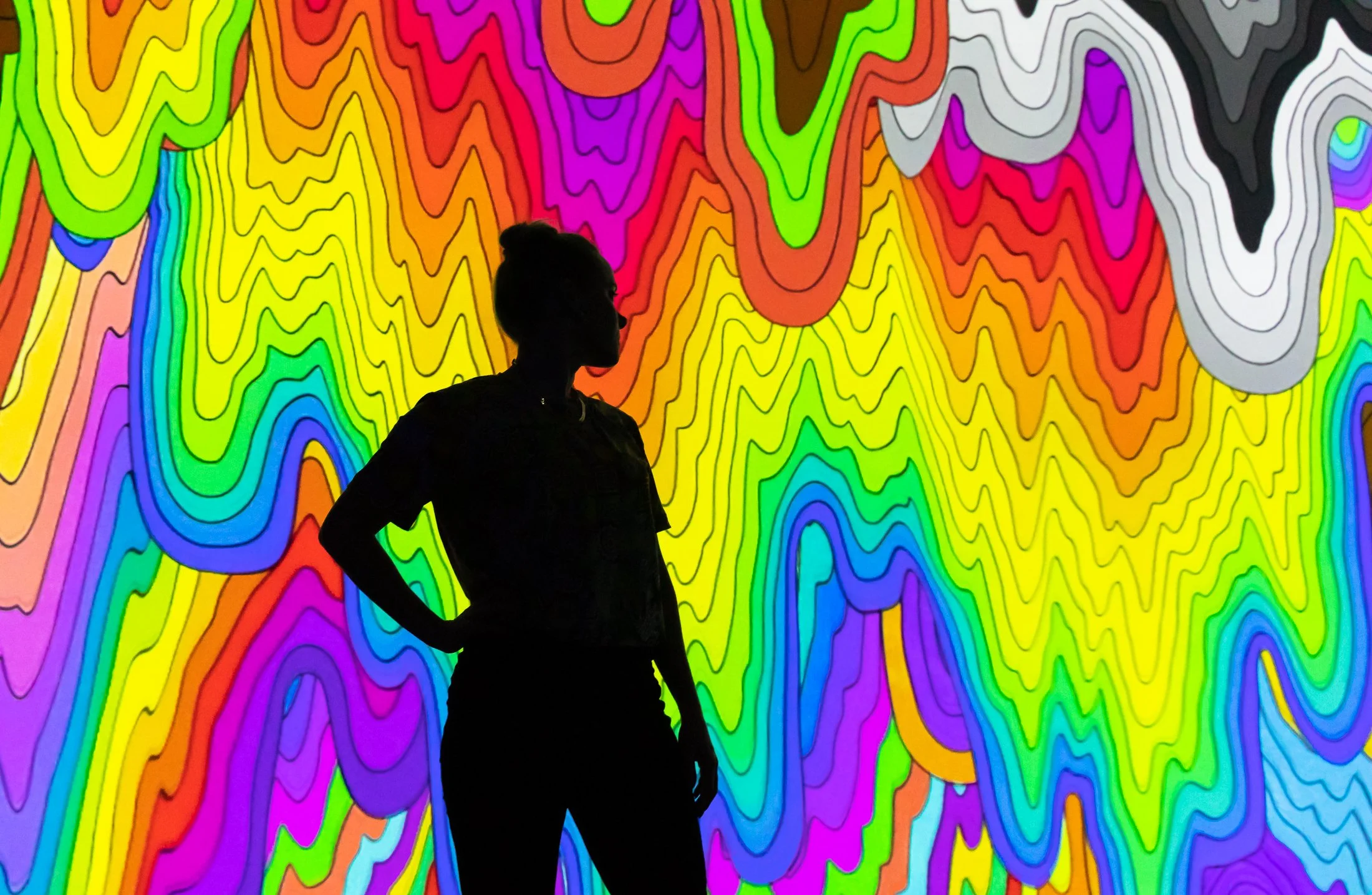 Silhouette of a person standing in front of a vibrant, colorful, psychedellic, abstract background with wavy lines.