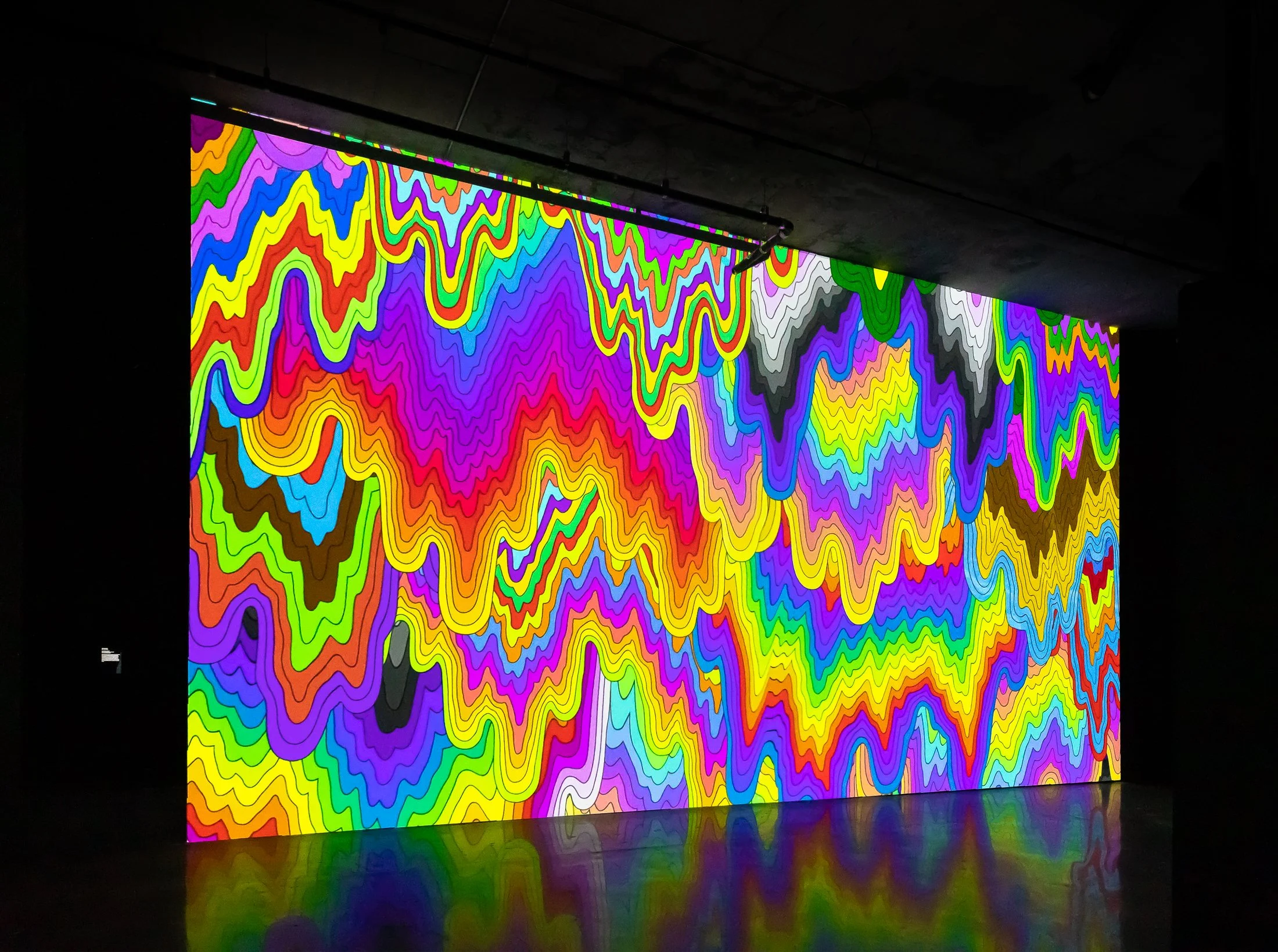 Immersive digital art display with vibrant, multicolored, abstract wavy lines in a dark room.