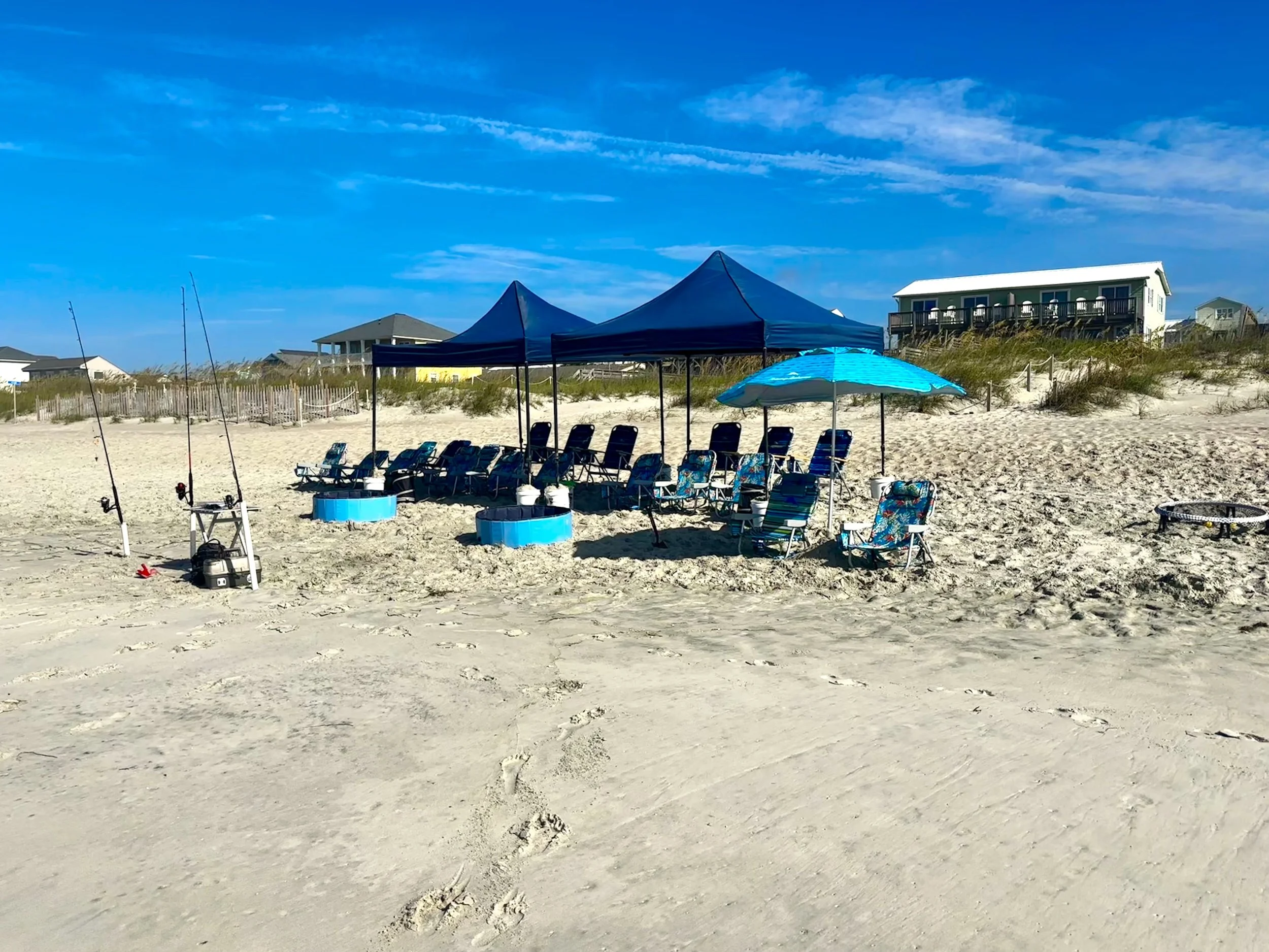 Beach setup with chairs, umbrellas, and fishing rods under a blue sky.