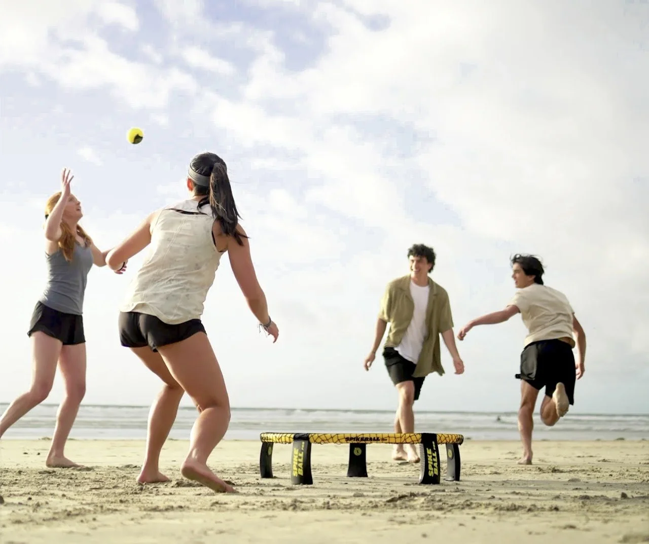 Five young people playing spikeball on the beach during the daytime.