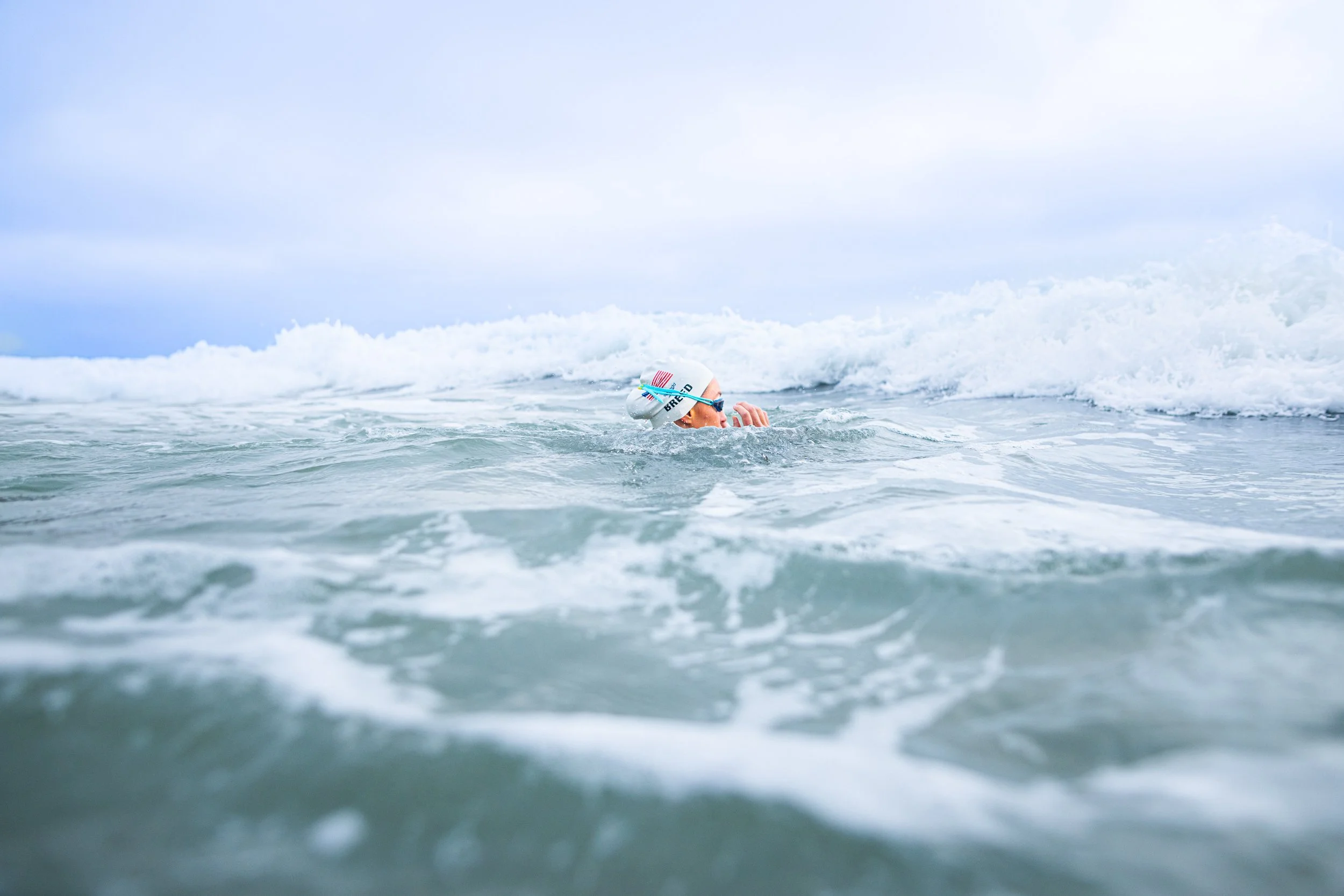 Person swimming in open water, wearing a cap and goggles.