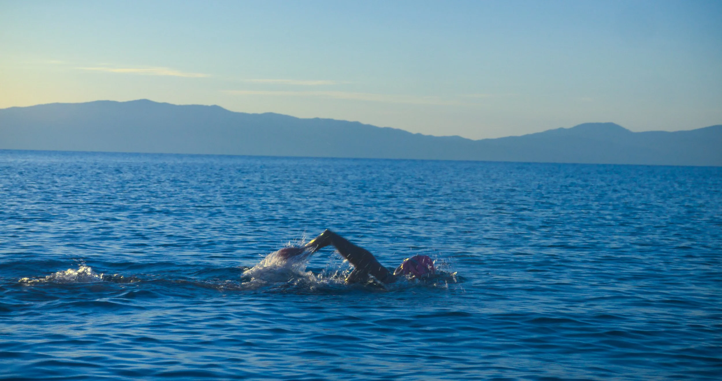 Swimmer performing open water swimming in a large body of water with mountains in the background.