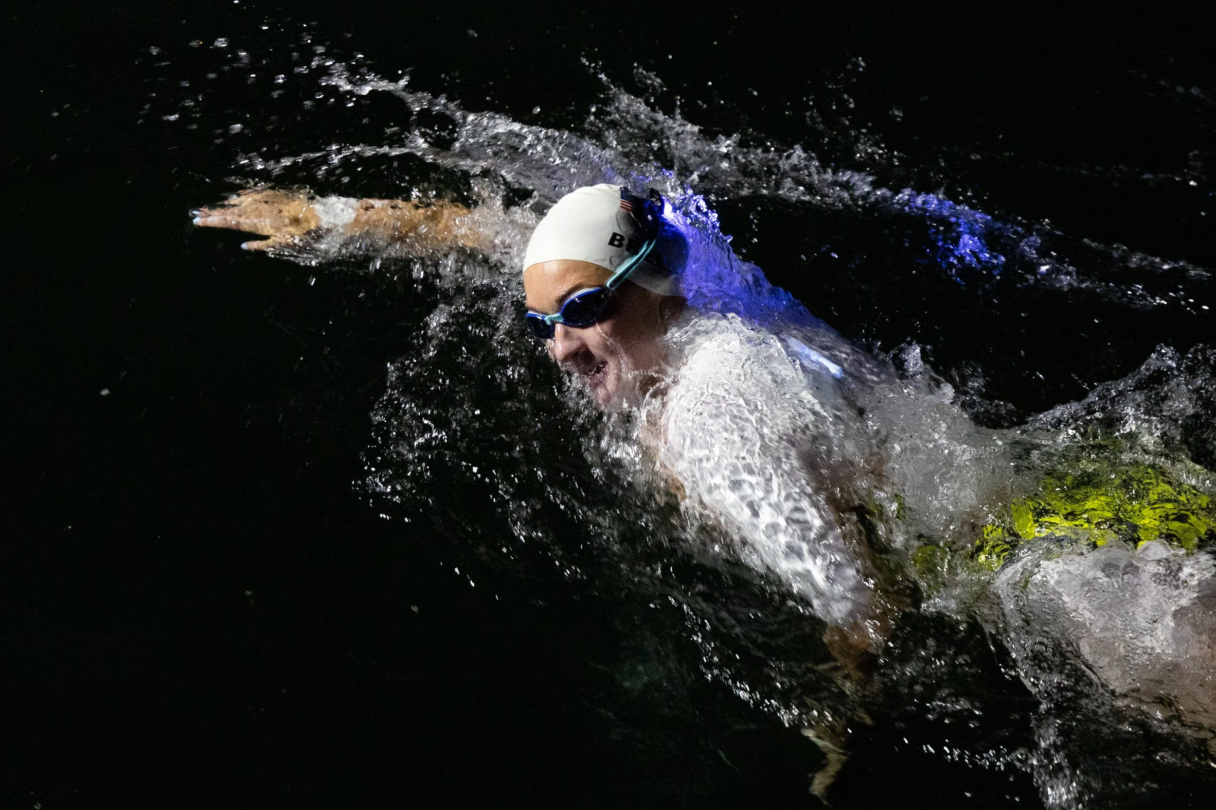 Swimmer wearing goggles and a swim cap, swimming in dark water at night.