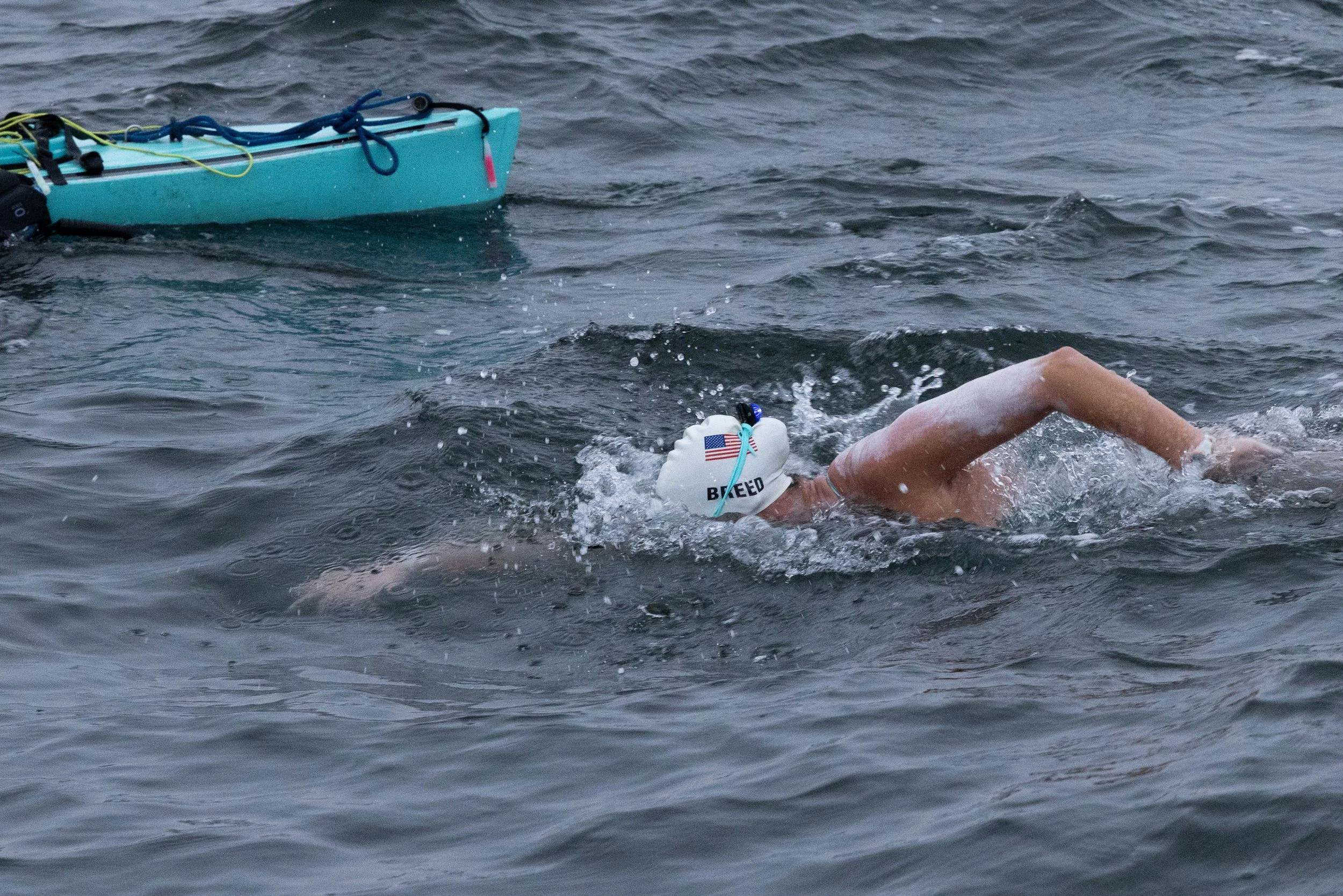 Swimmer in a white cap swimming in open water near a buoy or kayak.