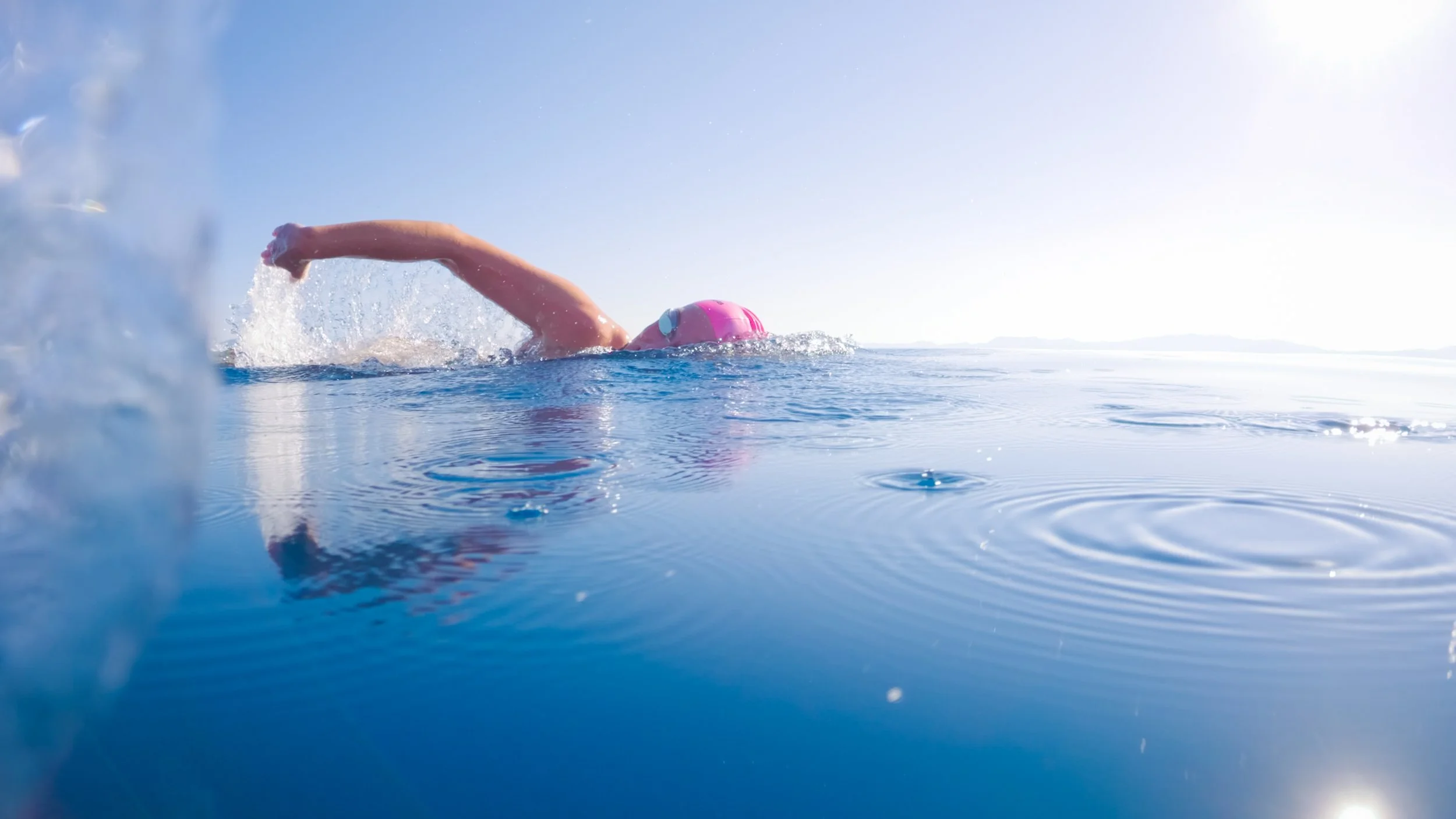 Swimmer in pink cap and goggles swimming in open water under bright sunlight
