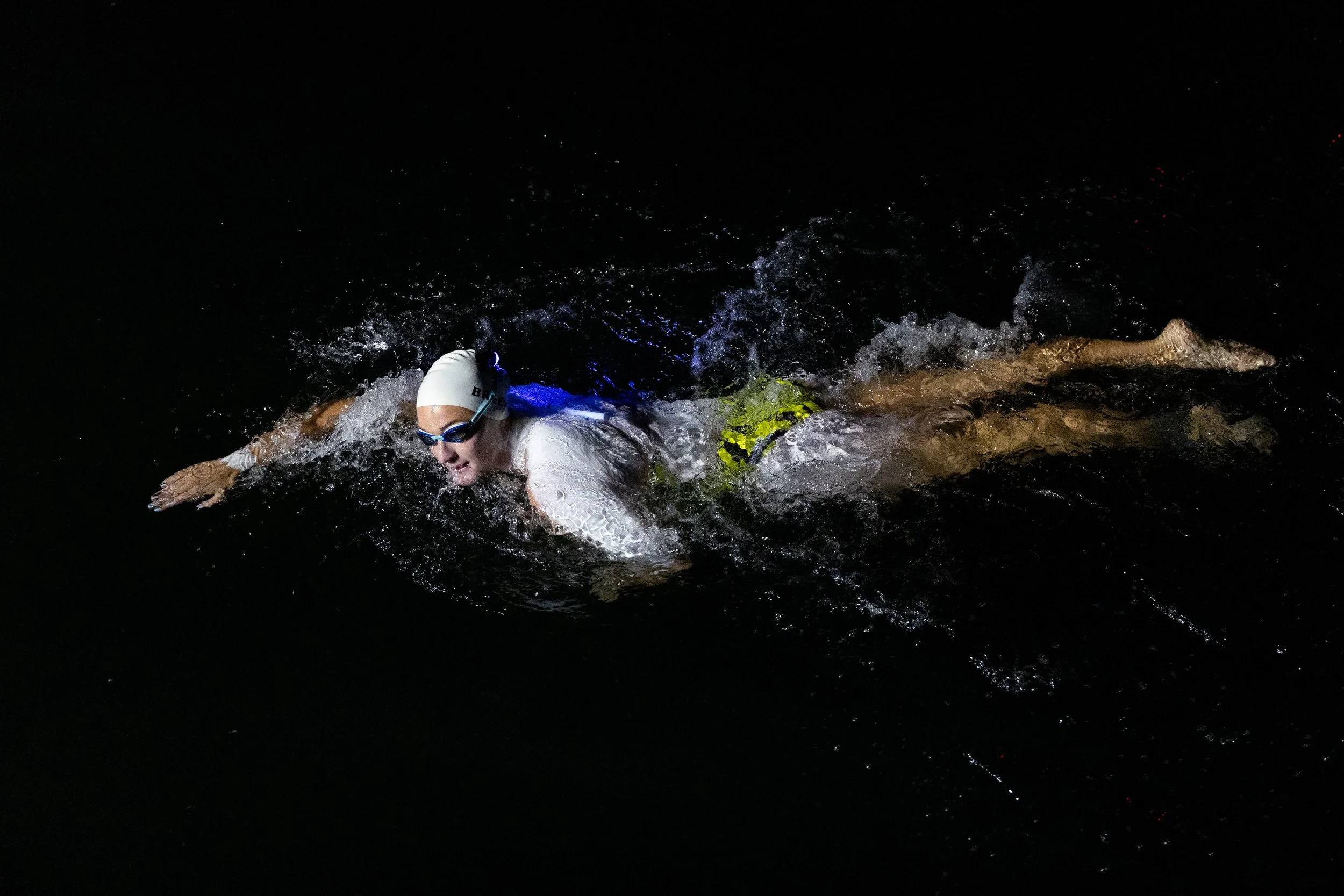 Swimmer in dark water wearing goggles and swim cap, performing freestyle stroke at night.