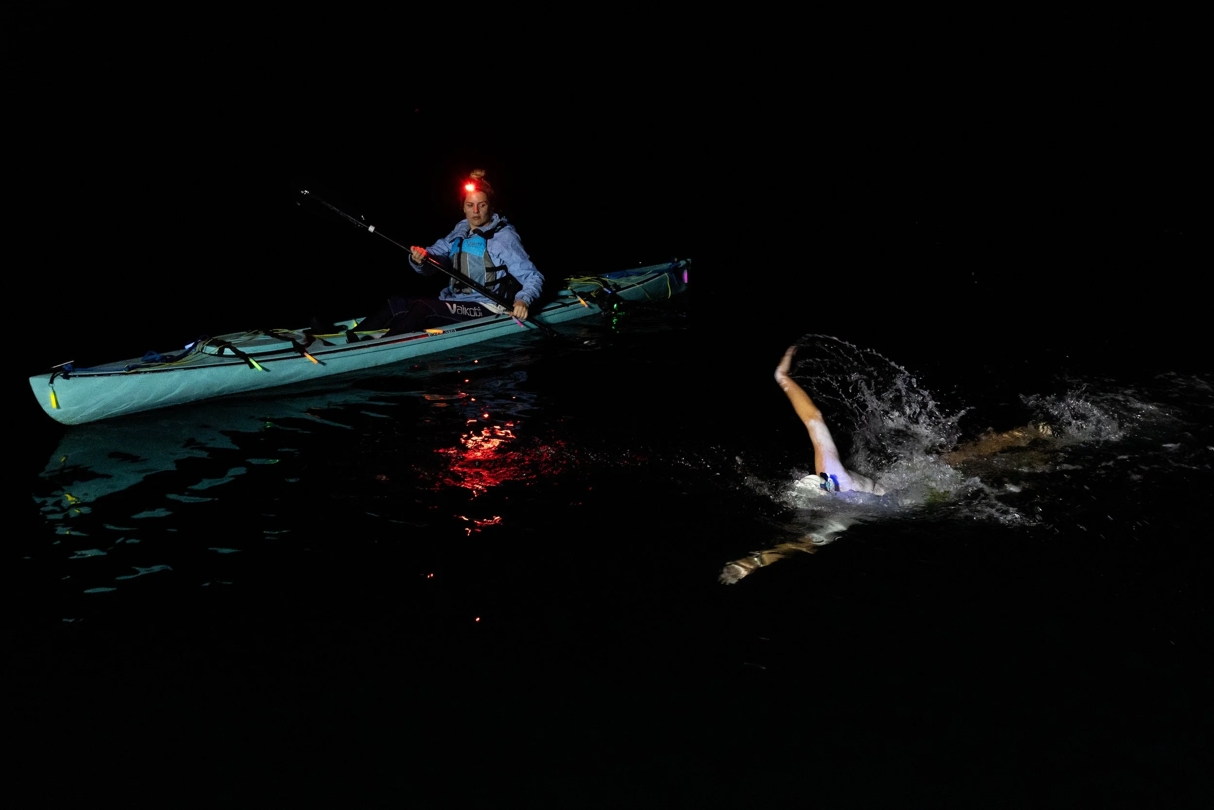 A person in a kayak night swimming with a headlamp on, practicing open water safety and rescue skills.