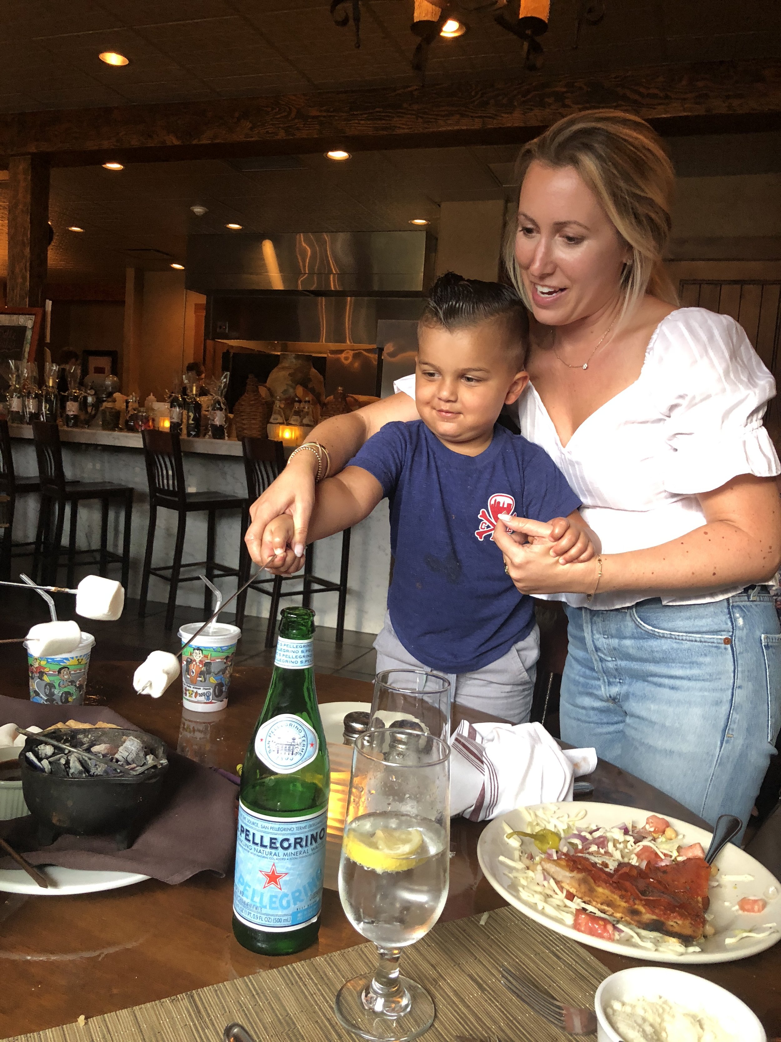 A woman and a young boy fireworks at a restaurant table, with food, drinks, and a bar in the background.
