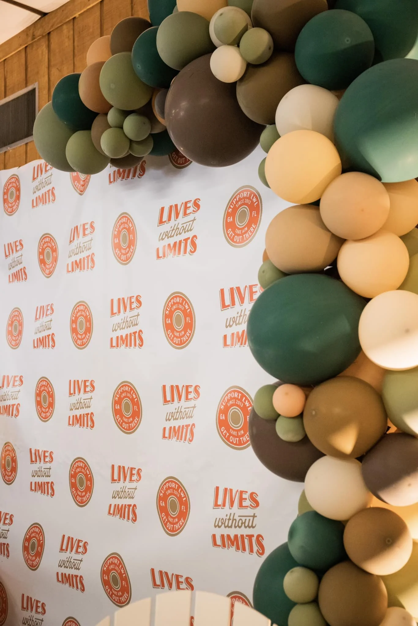 A colorful balloon arch with various shades of green, beige, and brown balloons, positioned in front of a backdrop that reads 'LIVES without LIMITS' and features circular logos with the text 'Support LIVES Georgia & FL since 2013, Get Out There'.