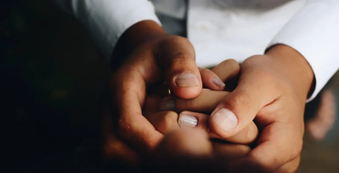 Two hands holding a small, cylindrical object, one hand appears to be that of a child, and the other that of an adult, dressed in a white shirt or lab coat.