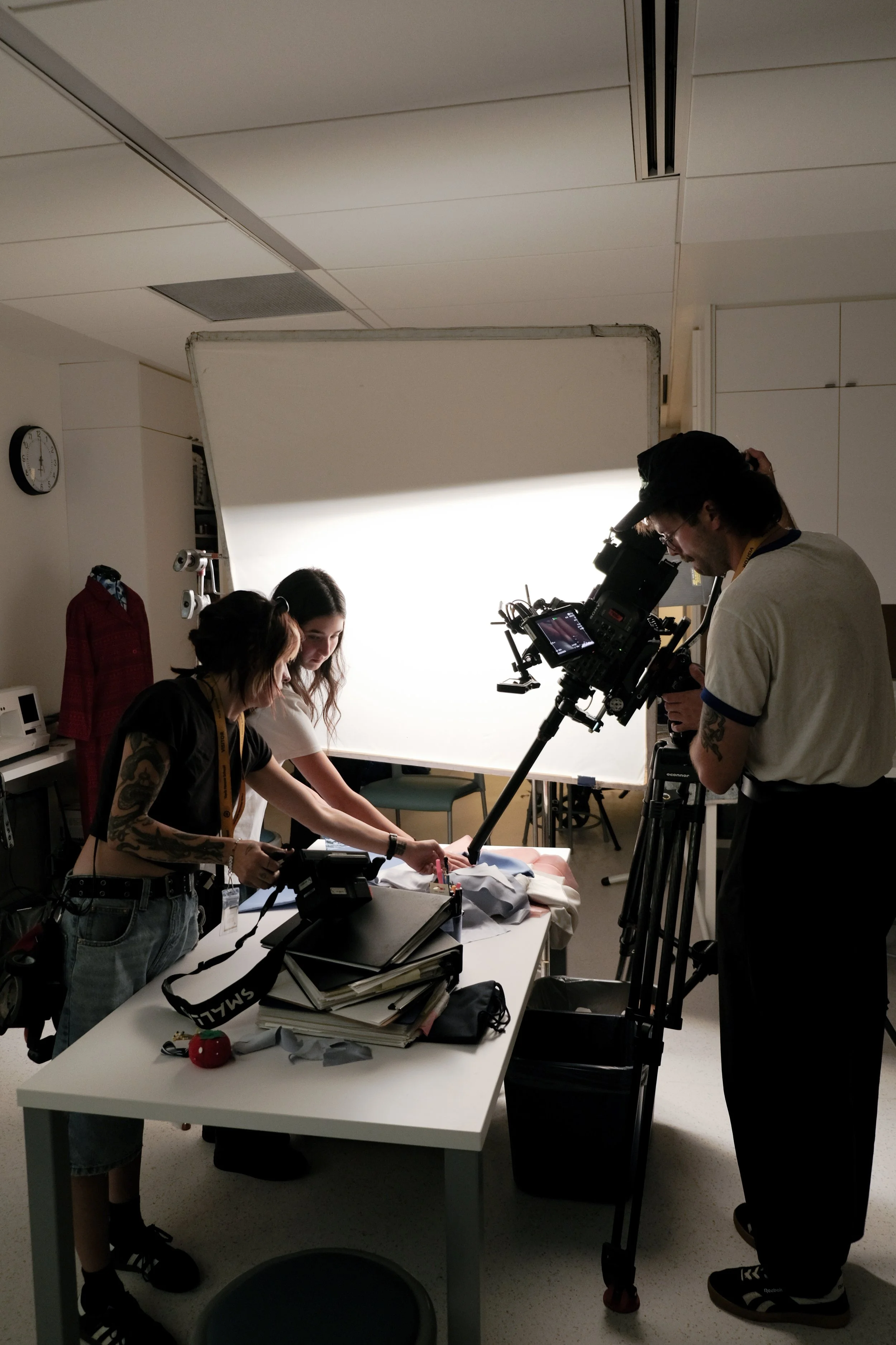 Filmmakers capturing footage of a clothing display against a white backdrop in a studio.