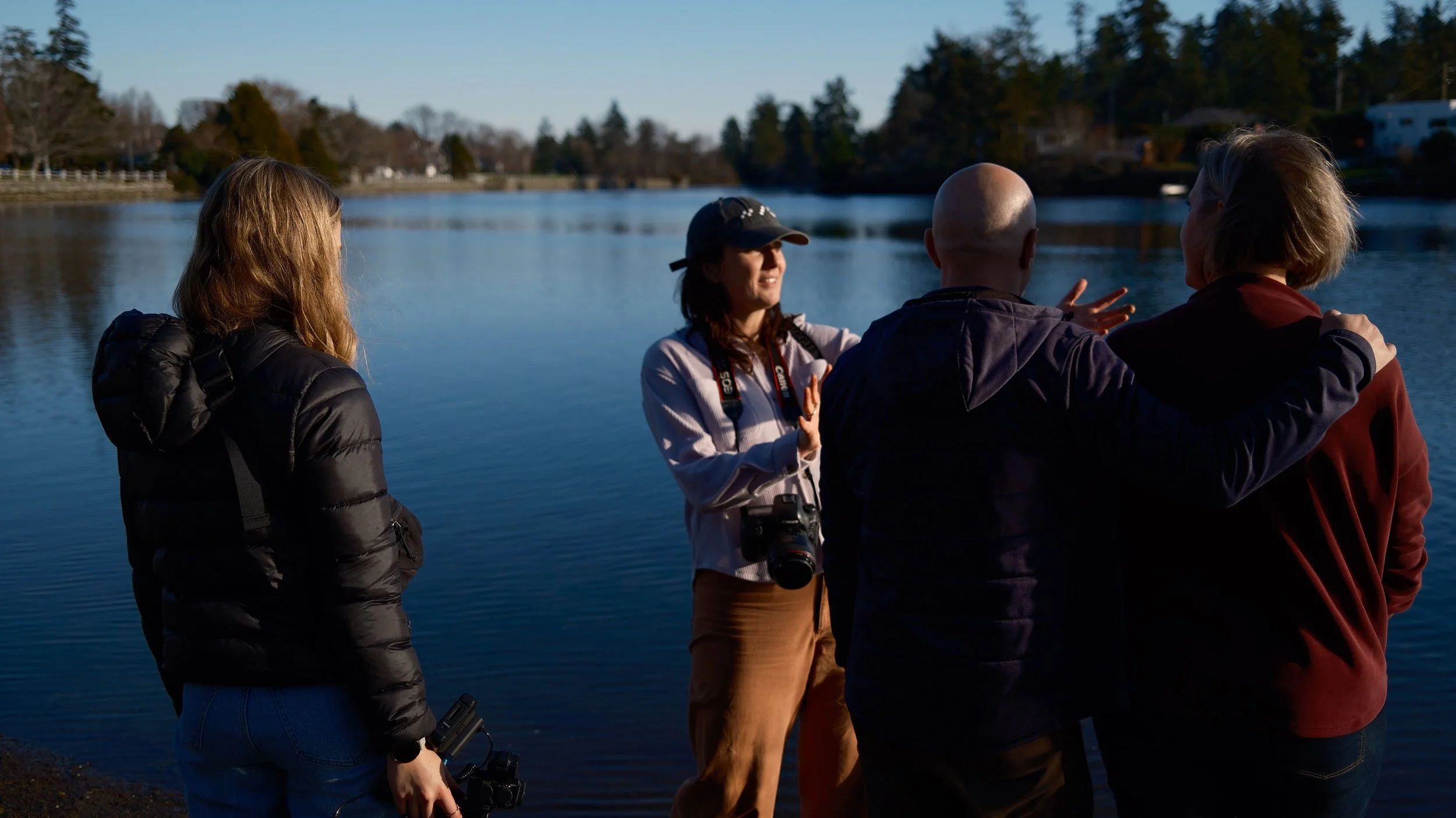 Four people standing by a lake, having a conversation during the daytime.