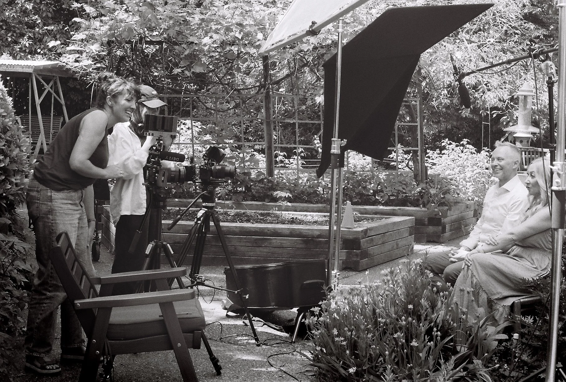 People filming an outdoor interview in a garden with professional camera, lighting, and sound equipment.