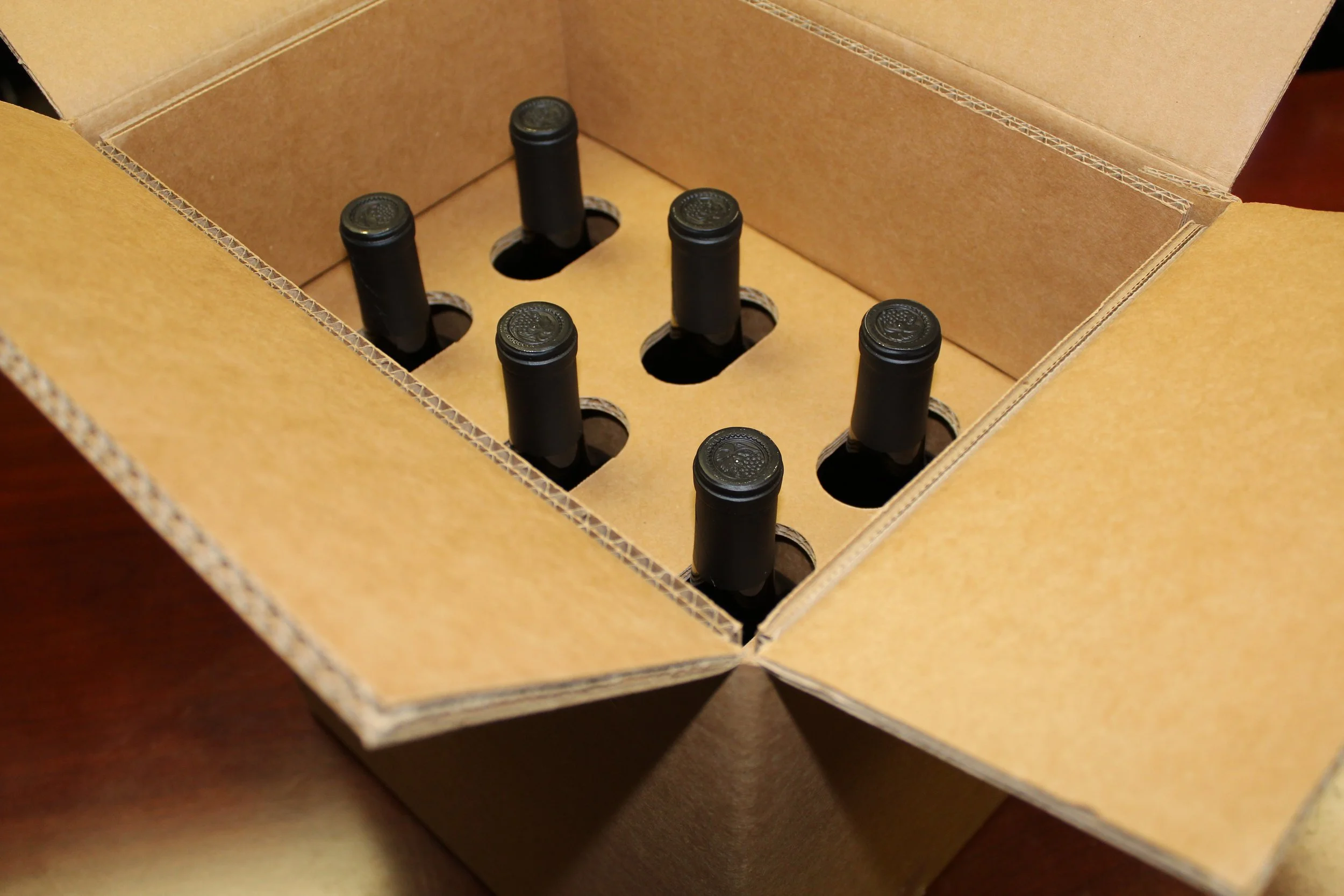 A cardboard shipping box with six wine bottles inside, each inserted into a separate slot.