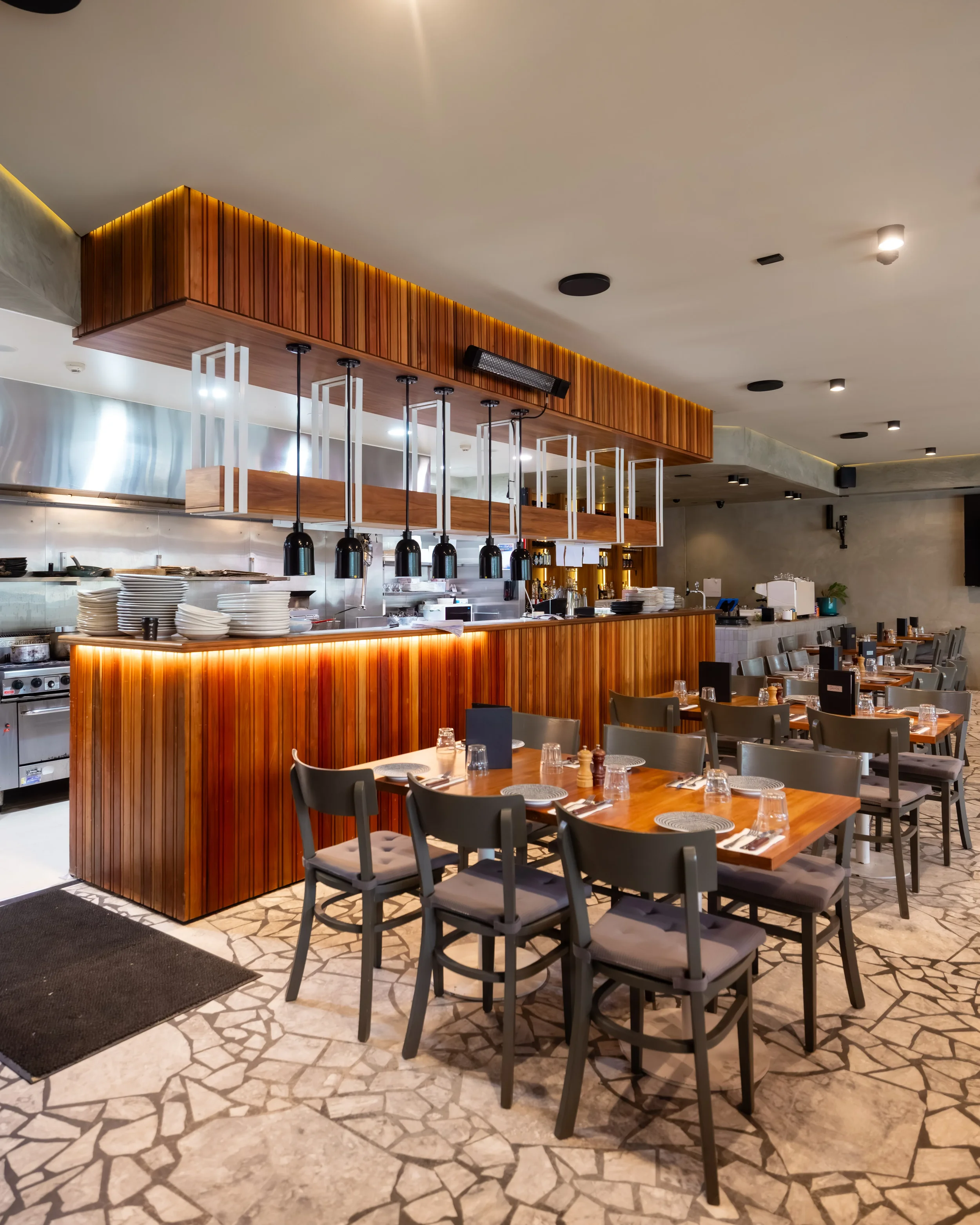 Interior view of a modern restaurant with a wooden bar and tables set with plates, glasses, and utensils.