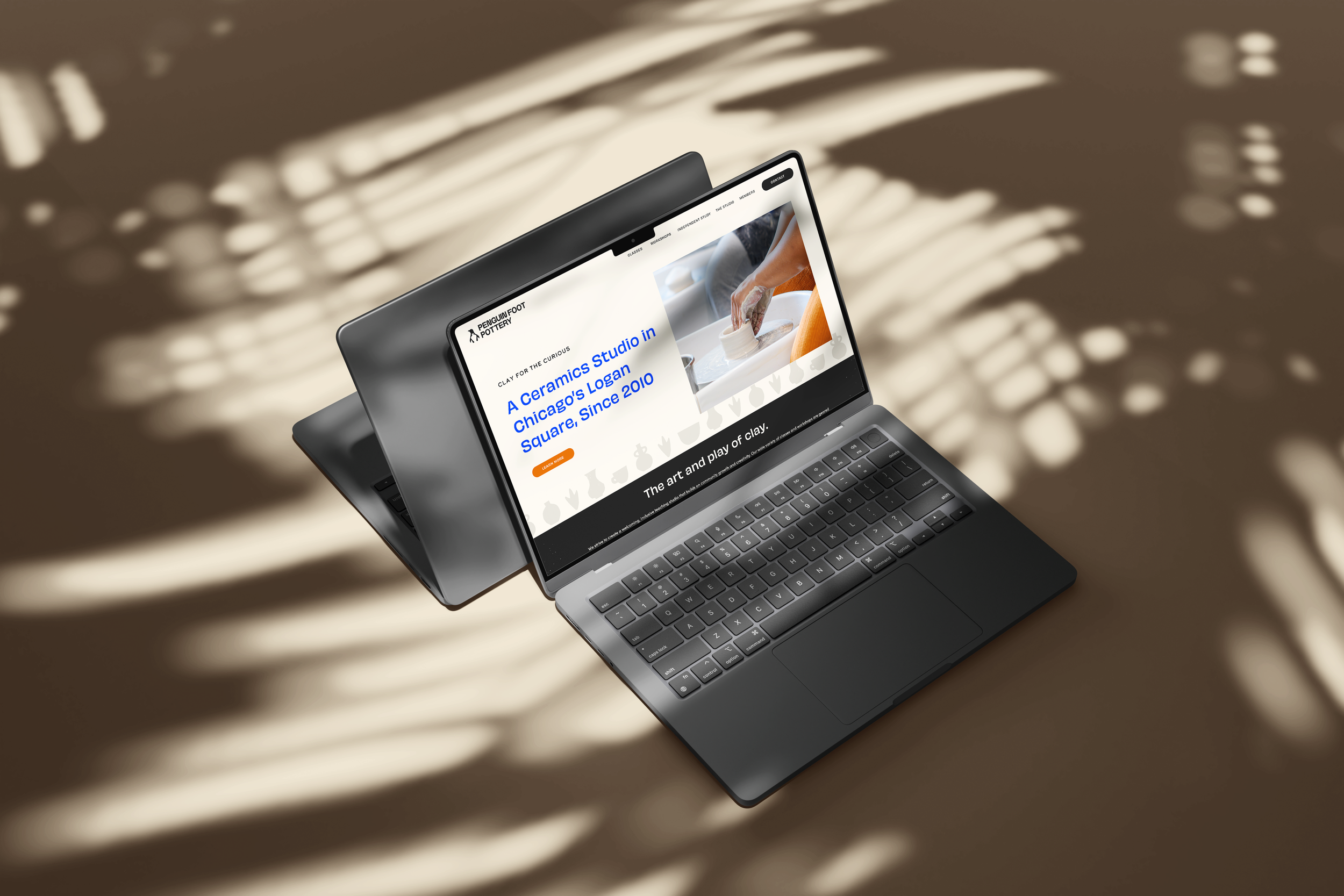A silver laptop with black keyboard displaying a website about a ceramic studio in Chicago, with shadows of leaves on a beige surface.