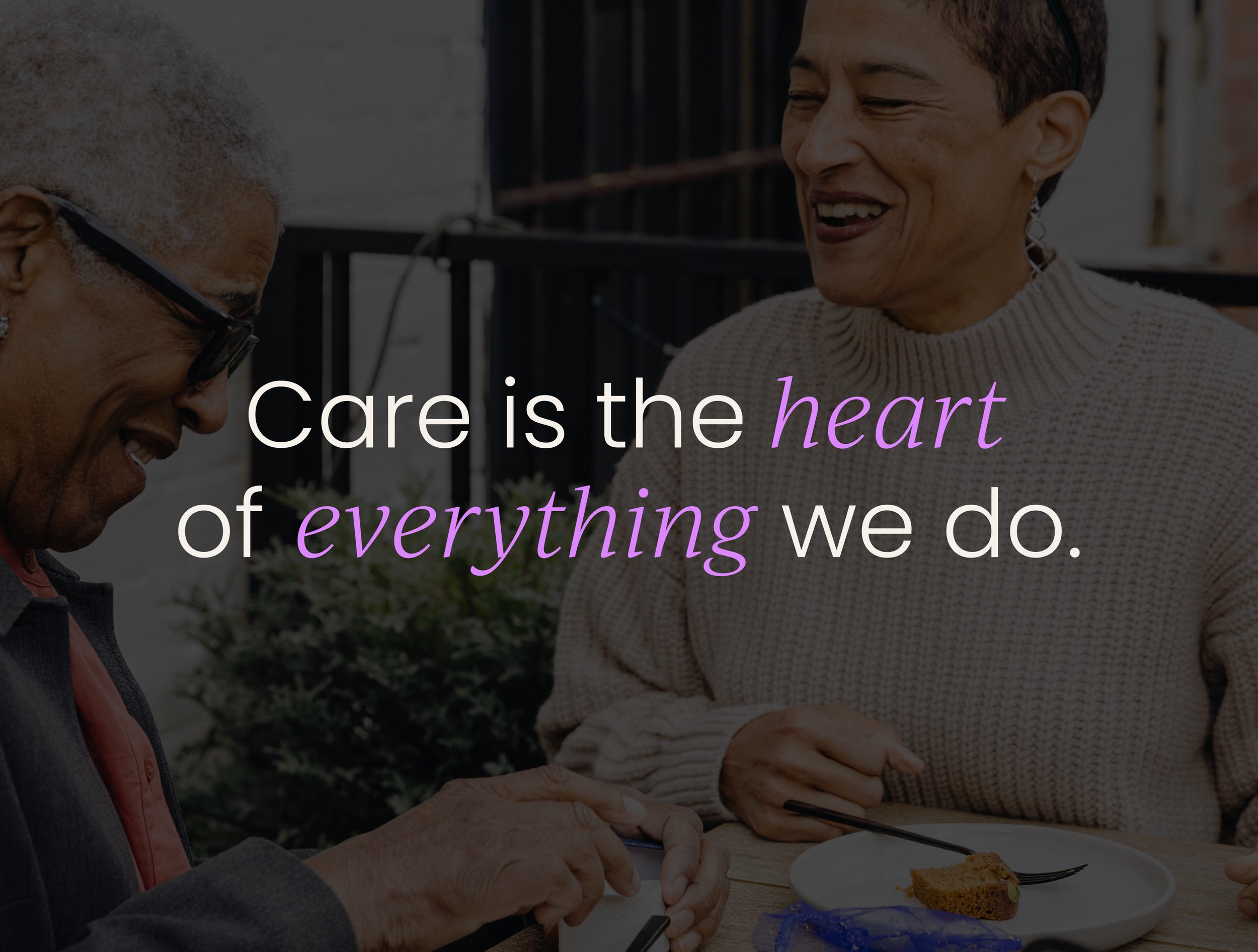 Two elderly women smiling and enjoying conversation at a table outside, one wearing glasses and the other with short hair and earrings, with a quote overlay that reads 'Care is the heart of everything we do.'